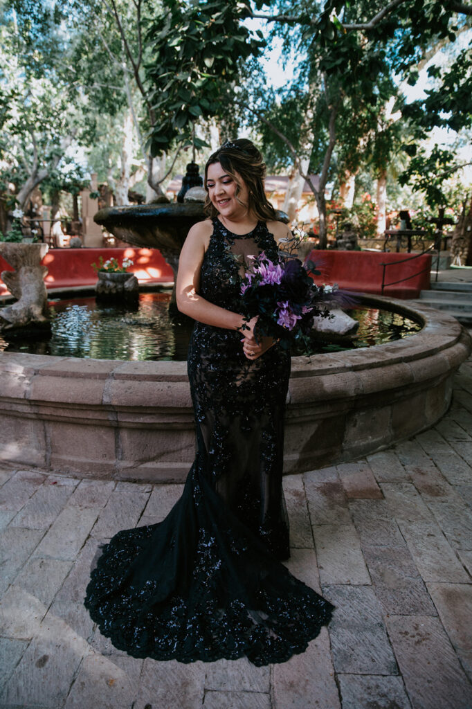 Bridal portrait in front of the courtyard fountain at boojum tree hidden gardens with a dramatic black wedding dress and colorful bouquet.
