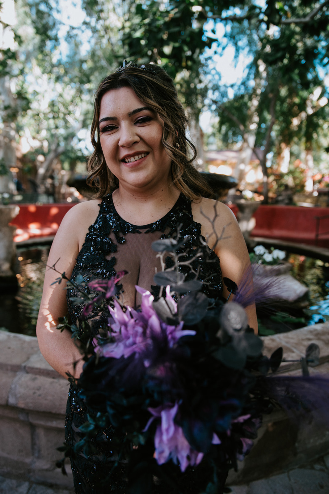Bride holding a purple and black bouquet in front of the fountain after the ceremony.
