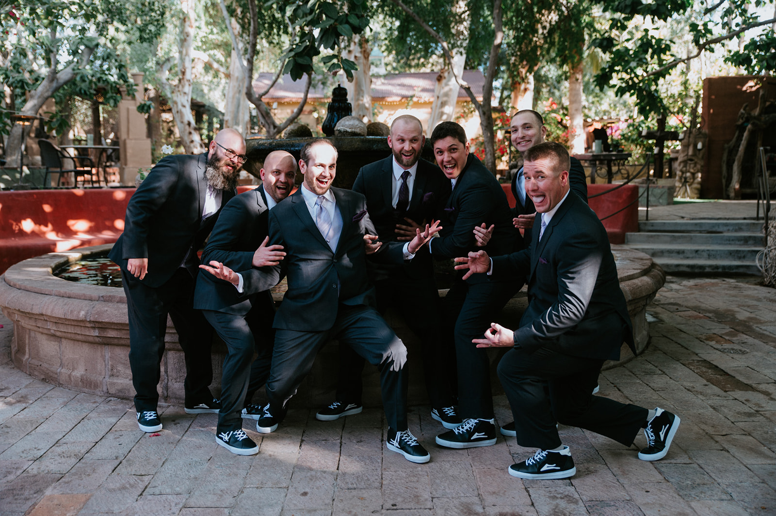 Groom and groomsmen posing with playful expressions beside the courtyard fountain at boojum tree hidden gardens.
