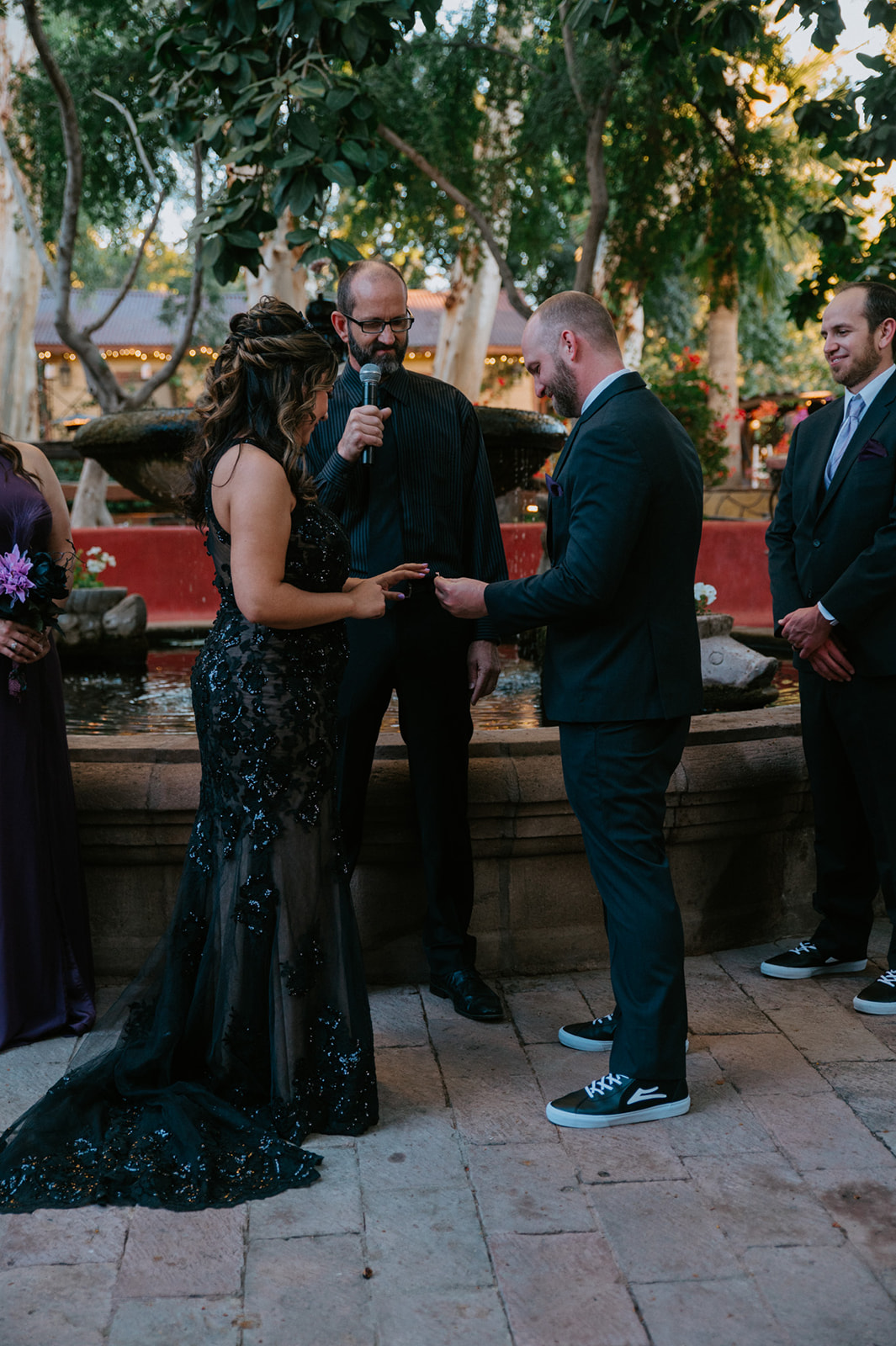 Groom placing a wedding band on the bride's finger during their boojum tree hidden gardens ceremony.
