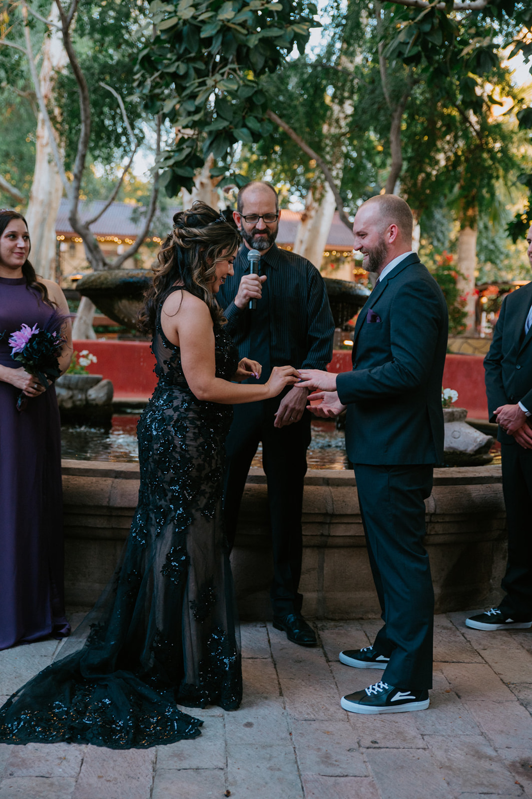 Bride placing a wedding ring on the groom's hand during their boojum tree hidden gardens wedding ceremony.

