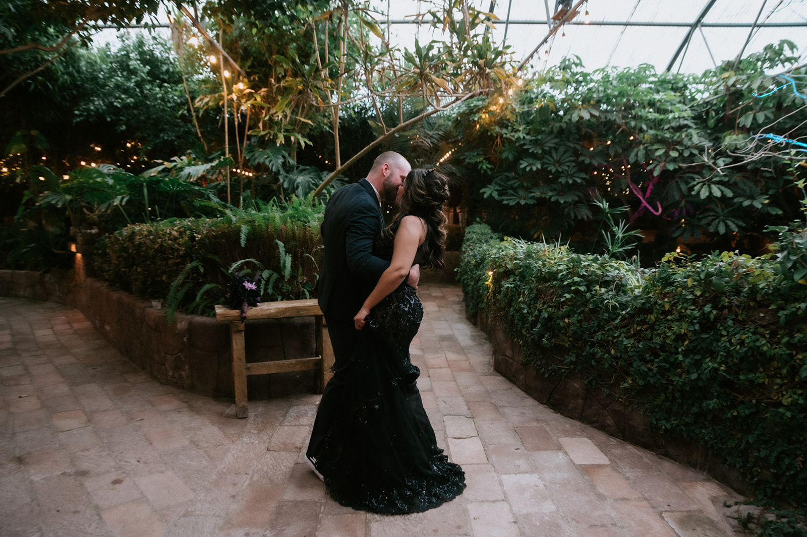 Bride and groom embracing in a greenhouse garden during their boojum tree hidden gardens wedding portraits.
