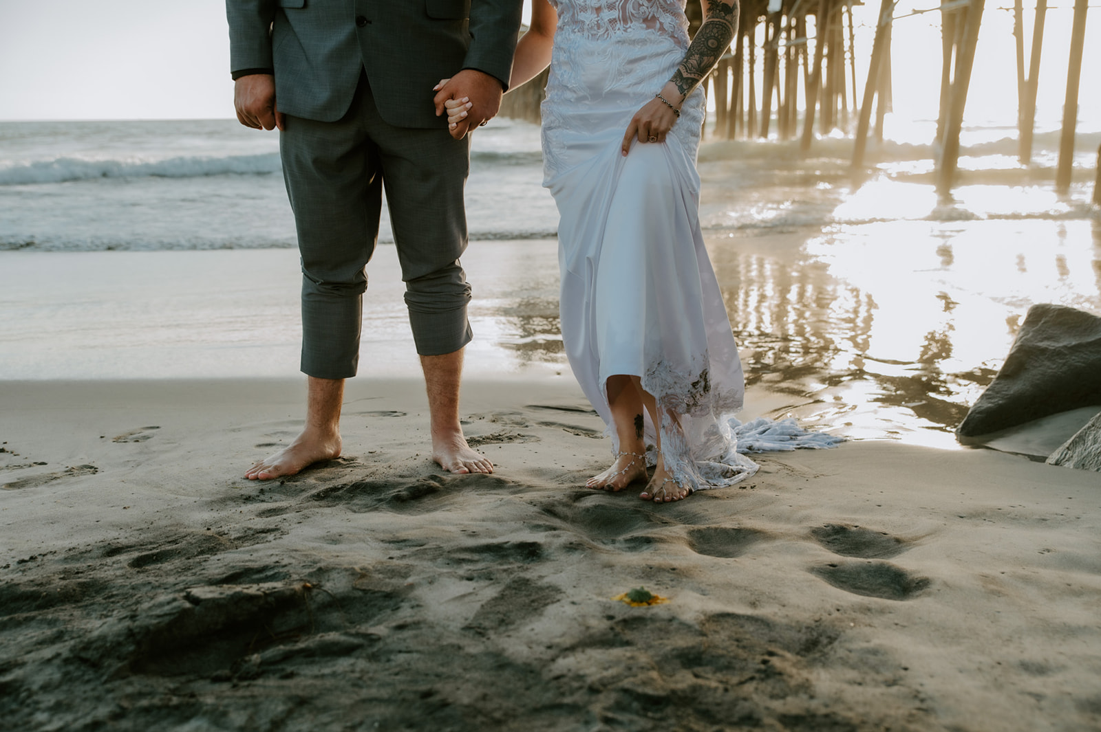 Couple standing barefoot on the beach near a pier during a California elopement, showing how to plan an elopement with family while still making space for intimate beach photos.
