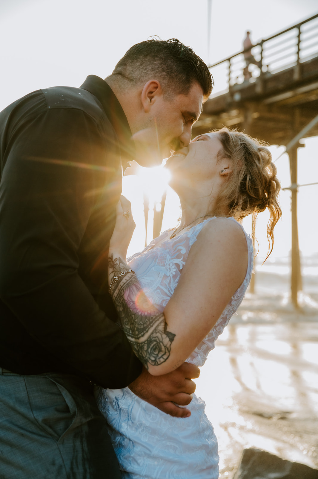 Intimate close-up of the couple kissing as sunlight flares through the pier during beach portraits.