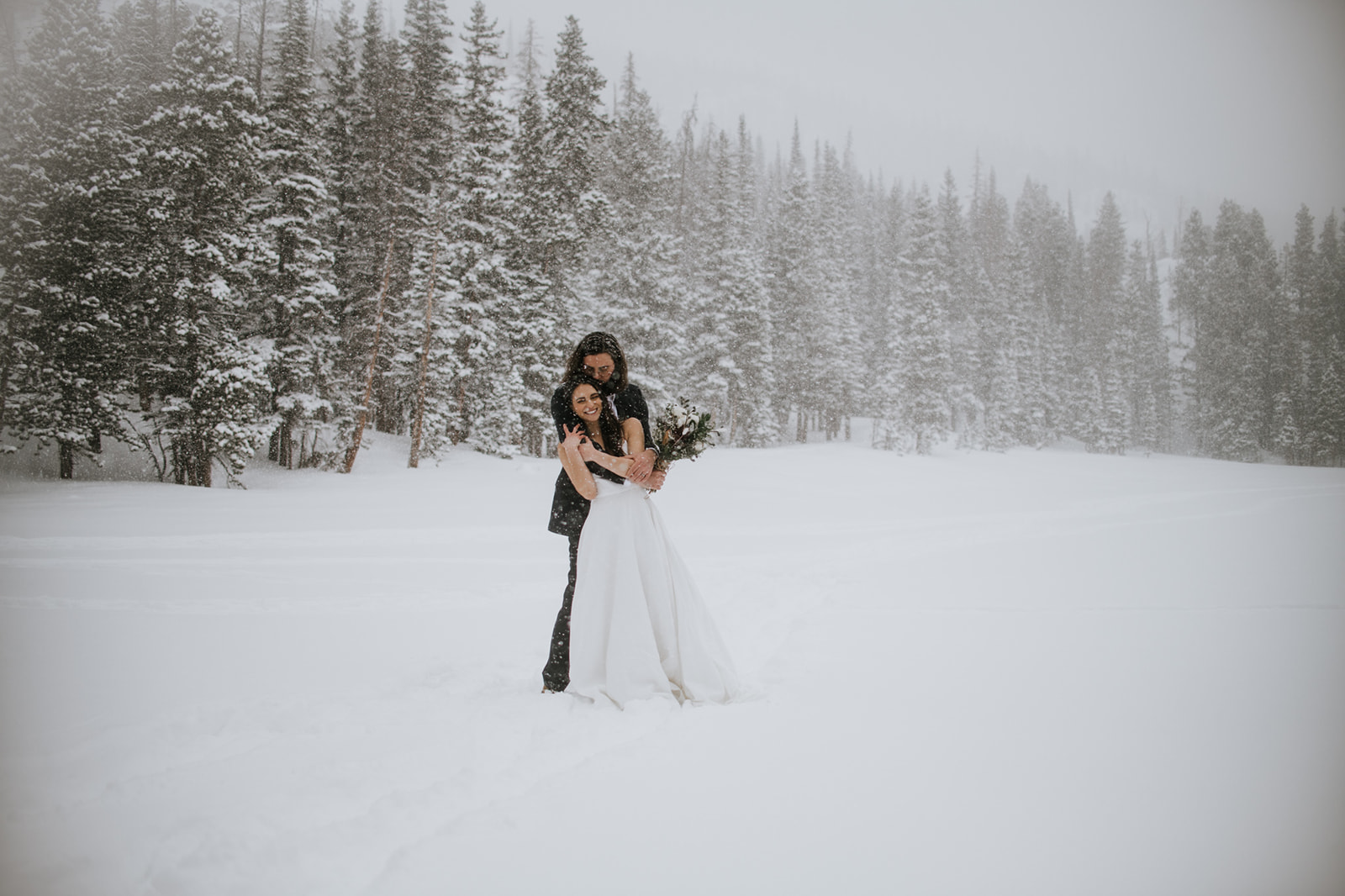 Wide shot of bride and groom standing together in deep snow during a rocky mountain national park elopement