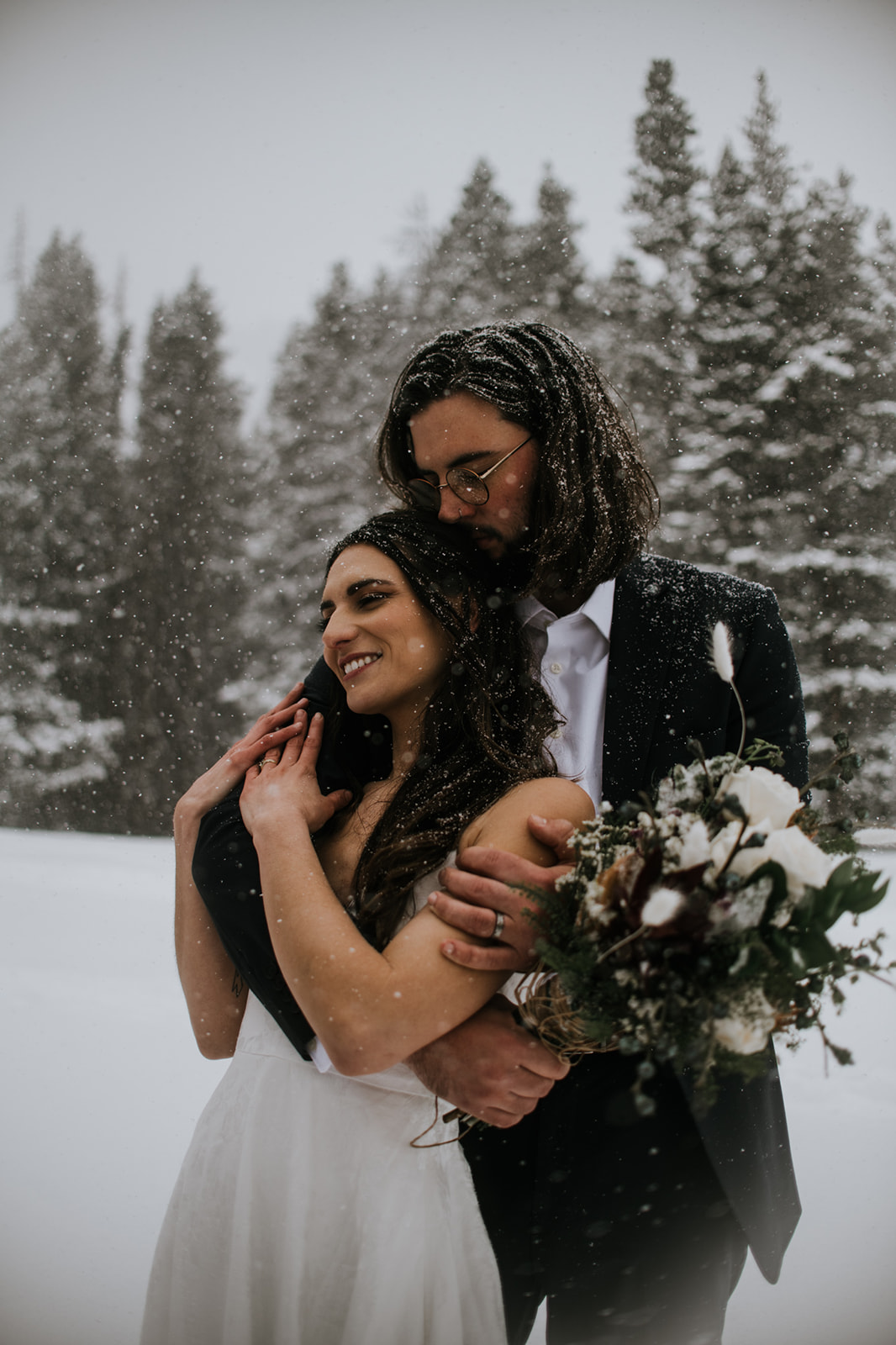 Groom hugging bride from behind as snow falls during a rocky mountain national park elopement