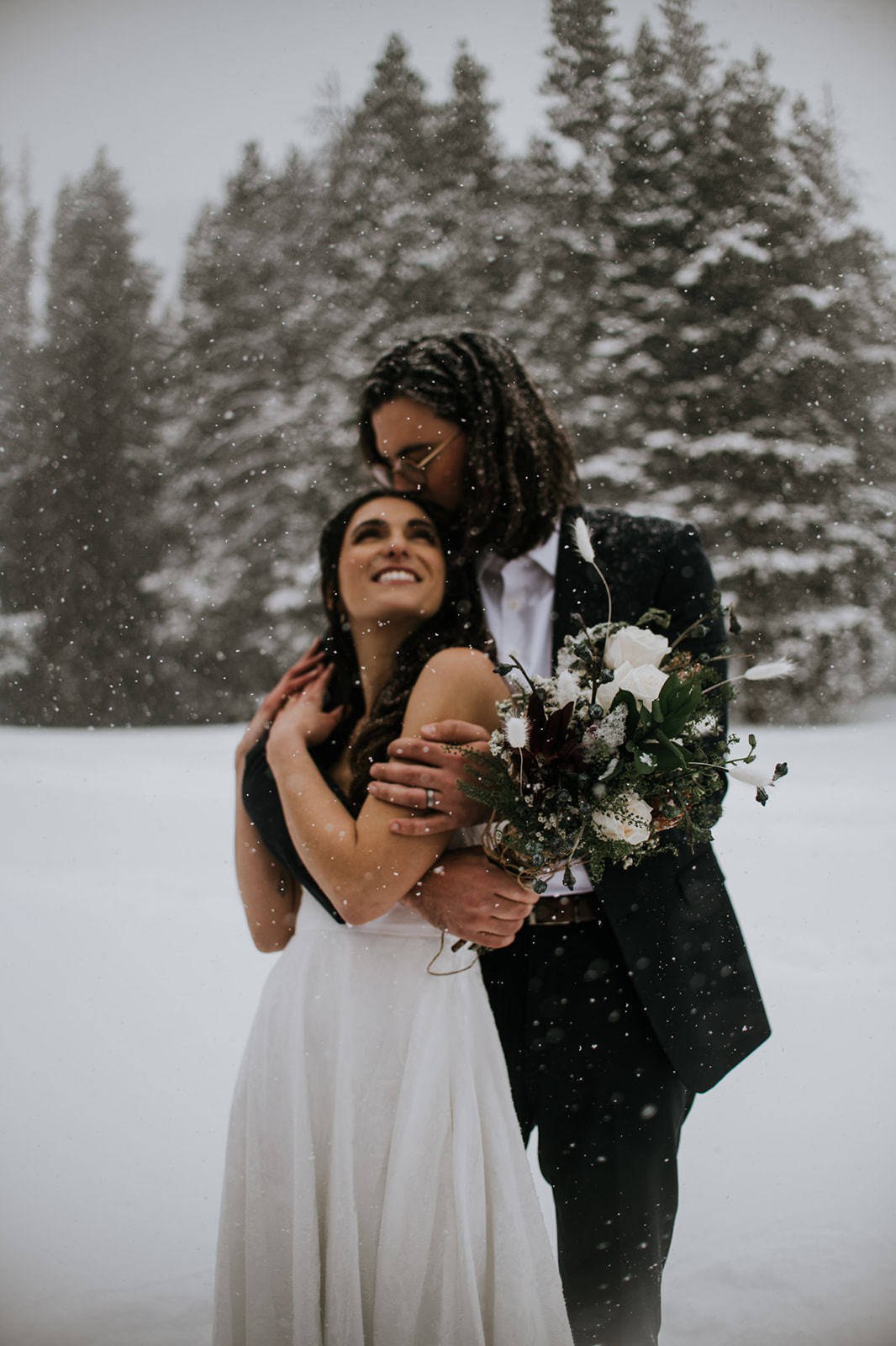 Bride leaning into groom in a quiet forest during a rocky mountain national park elopement in winter