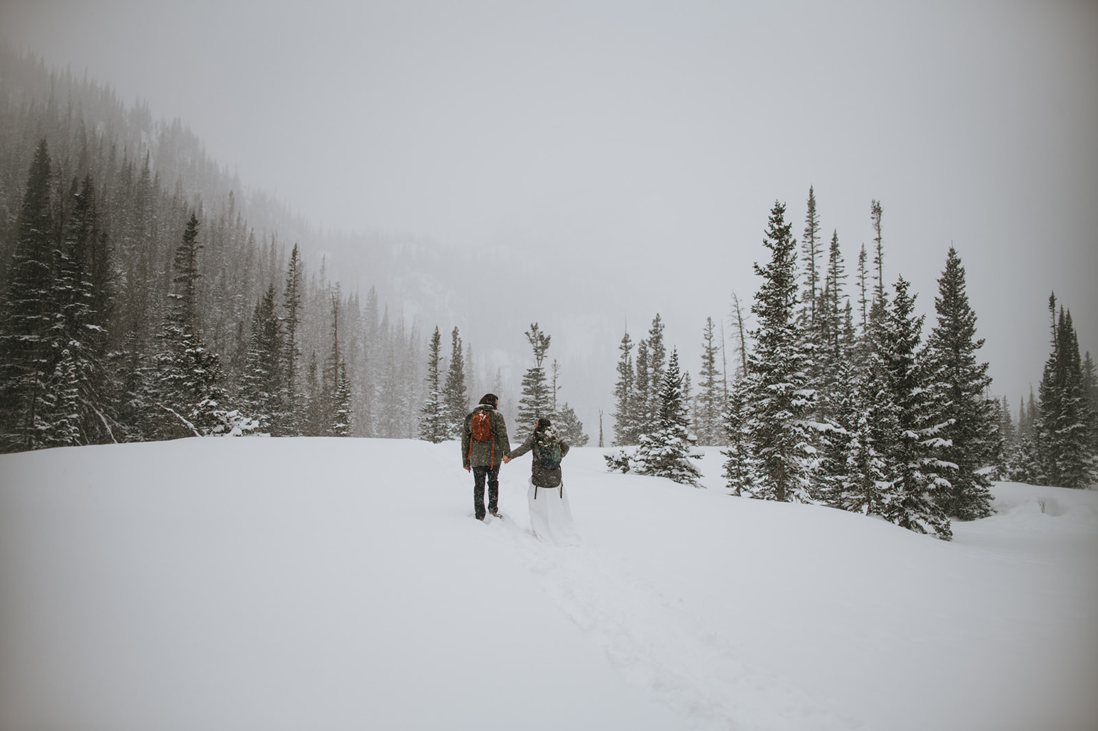 Couple walking hand in hand through fresh snow during a rocky mountain national park elopement in a snowstorm