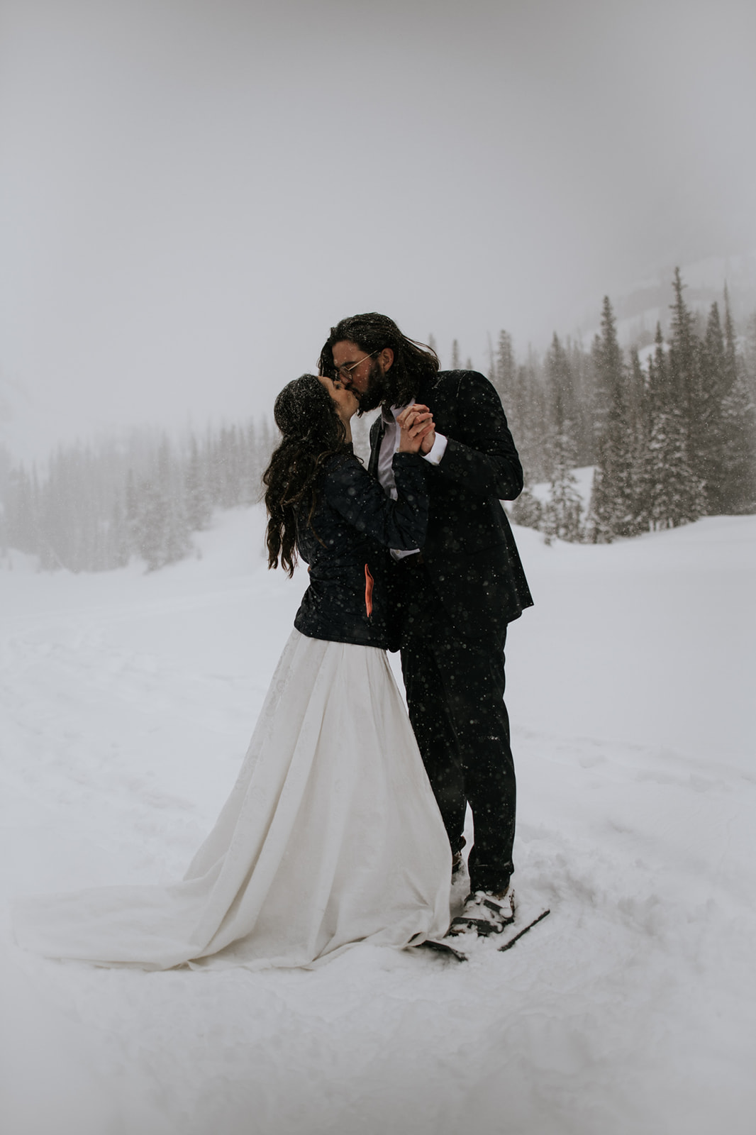 Couple sharing a quiet kiss in falling snow during a winter elopement in the mountains