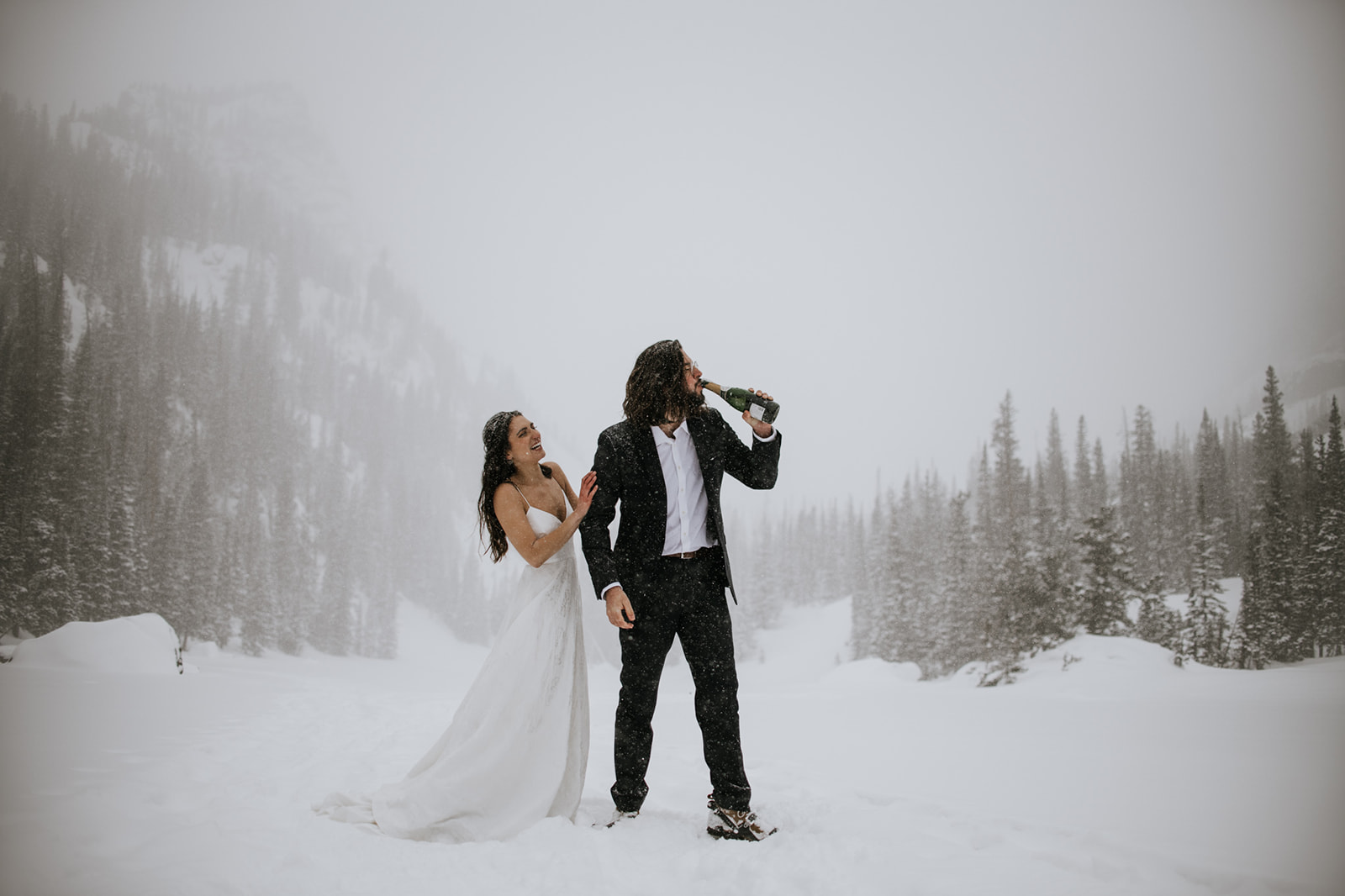 Bride reaching for groom as he drinks champagne during a rocky mountain national park elopement celebration
