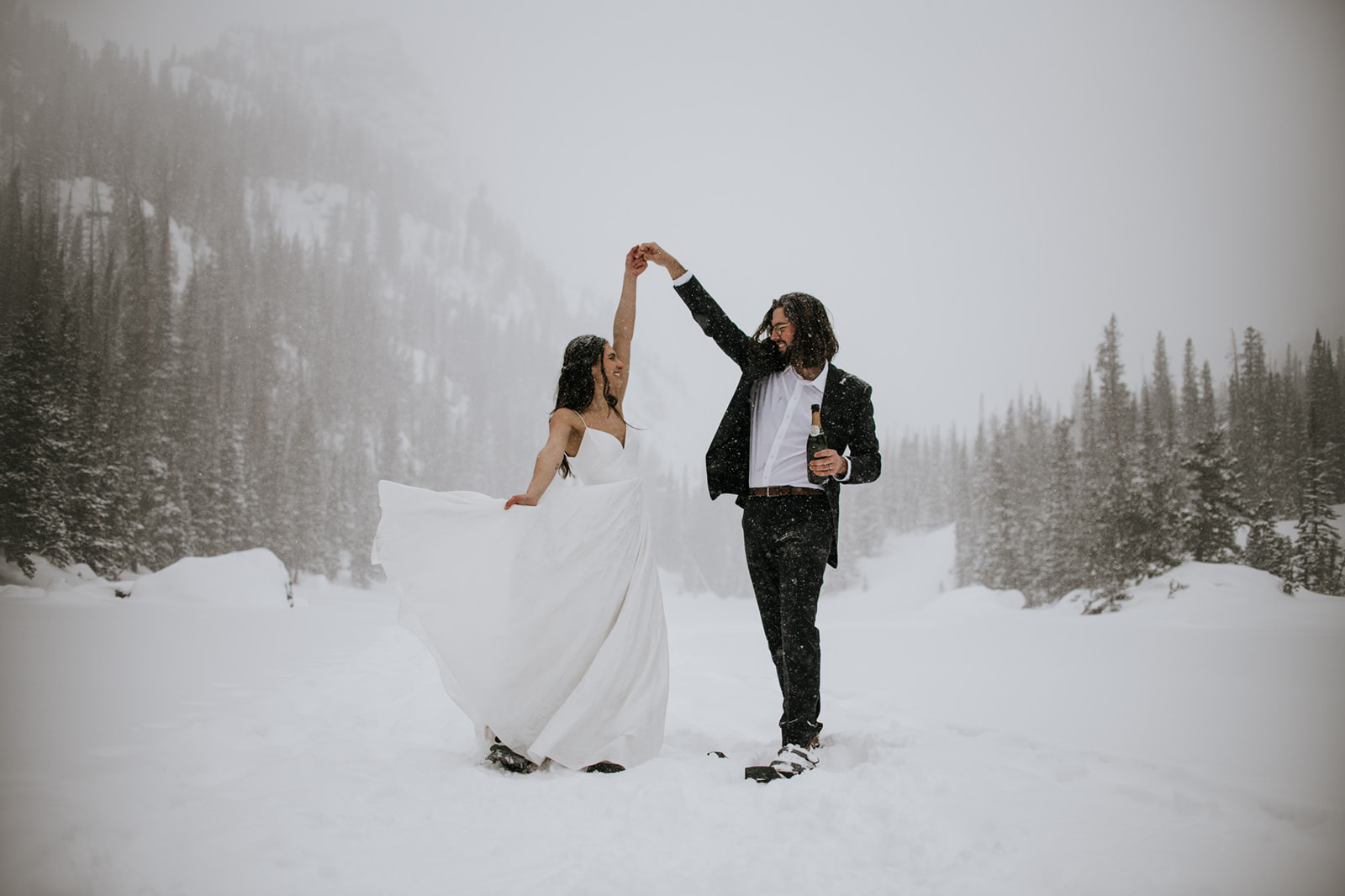 Bride twirling in her wedding dress as groom lifts her hand during a snowy winter elopement