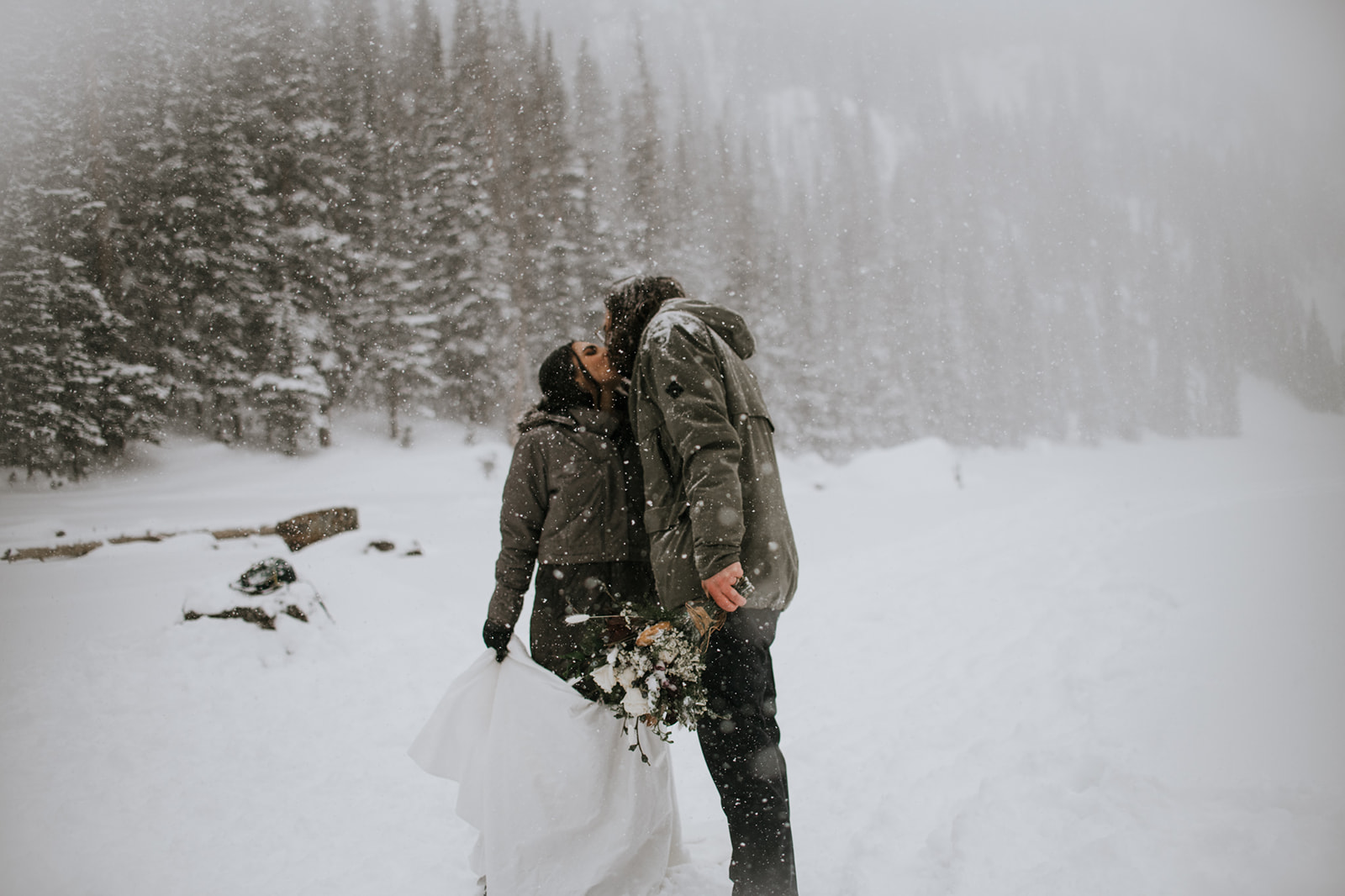 Close-up of bride and groom holding each other during a snowy mountain elopement, showing wedding rings and emotion