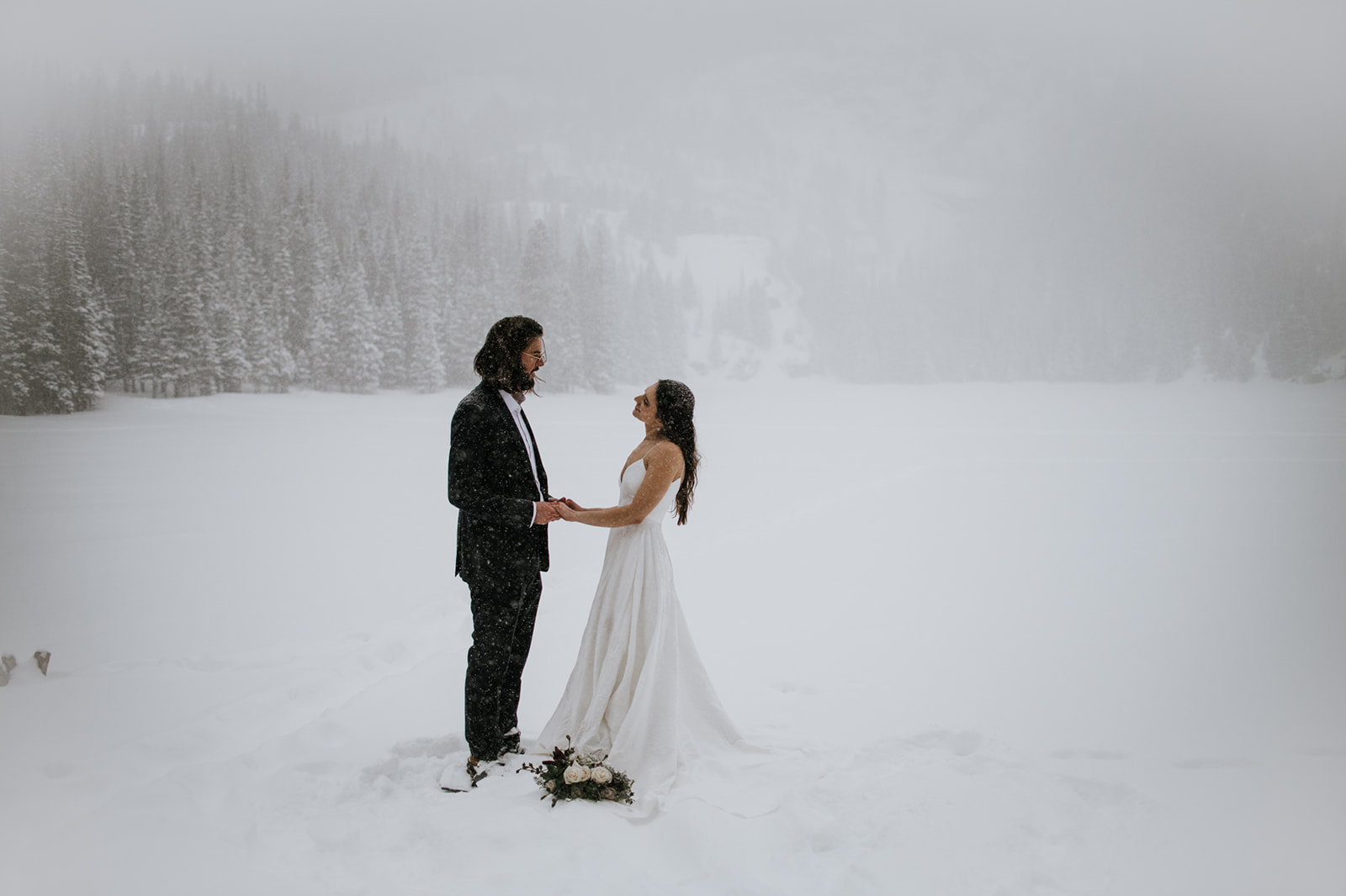 Bride and groom holding hands and smiling at each other during a rocky mountain national park elopement in snow