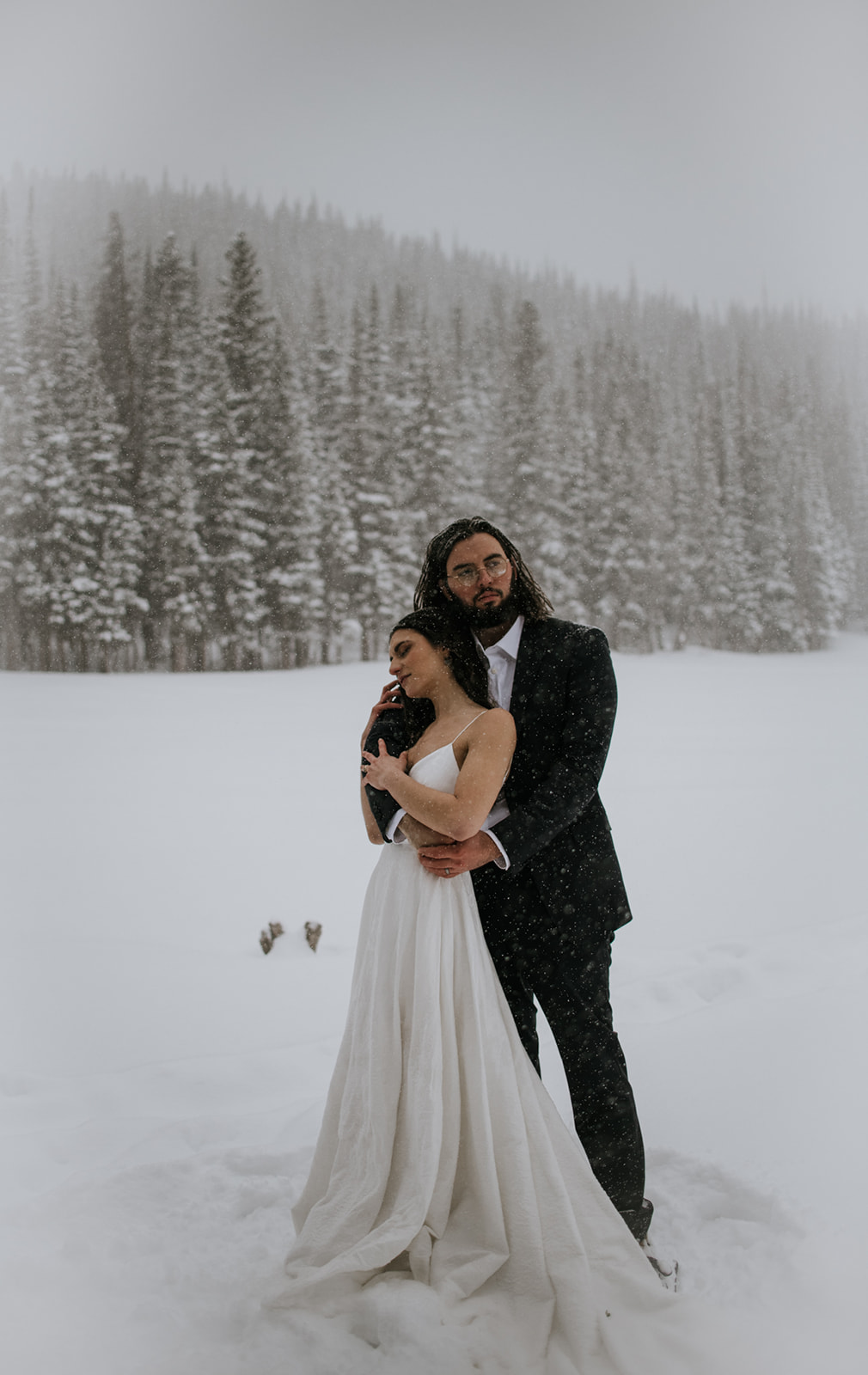 Groom wrapping his arms around bride as snow falls during a winter elopement in Rocky Mountain National Park