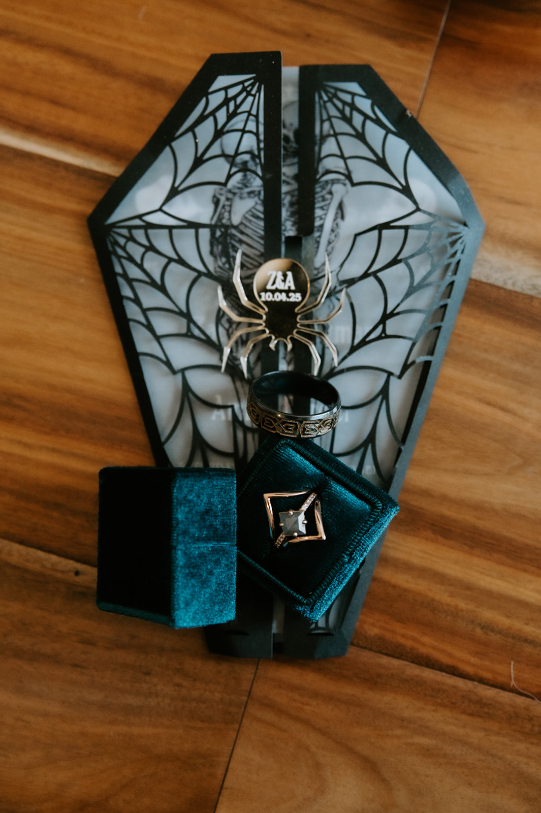 Flat lay of coffin-shaped wedding invitations, rings, and spider details on a wooden table for a California elopement with personal, nontraditional touches.