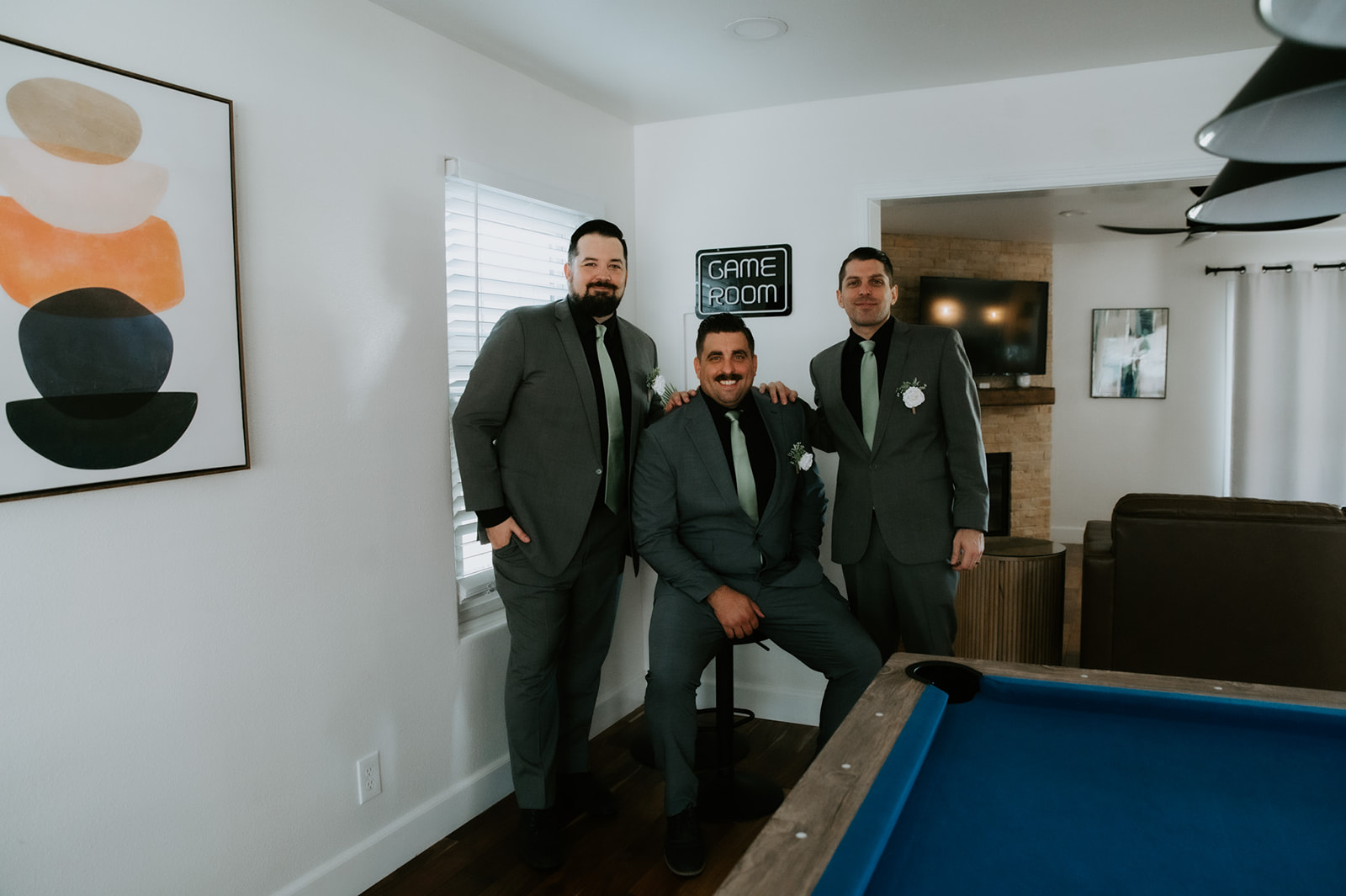 Groom standing with his groomsmen in a modern Airbnb game room, relaxed and laughing during a family-inclusive elopement morning.