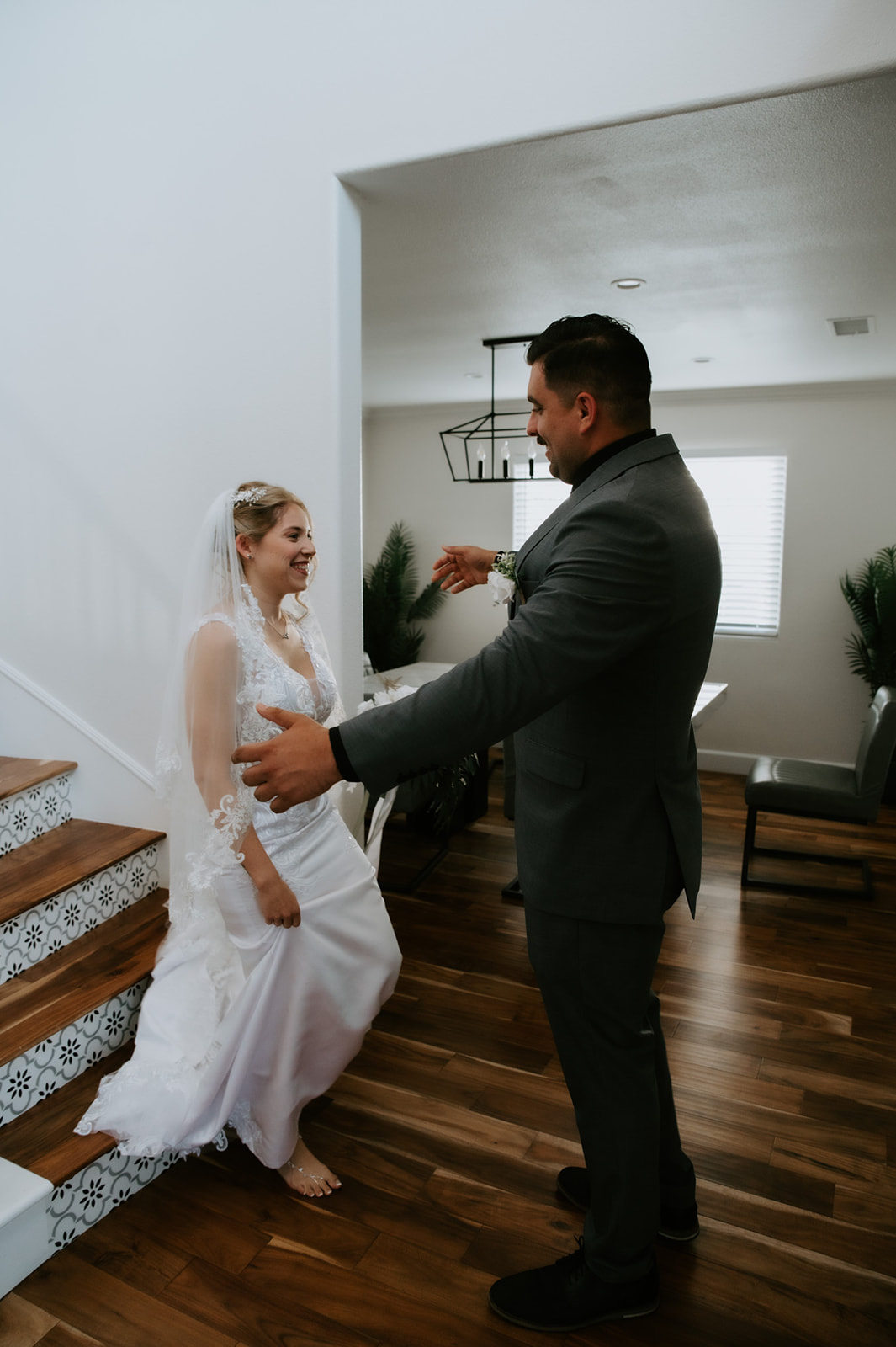 Groom opening his arms as the bride reaches the bottom of the stairs, a private first look during an Airbnb wedding planned with family present.