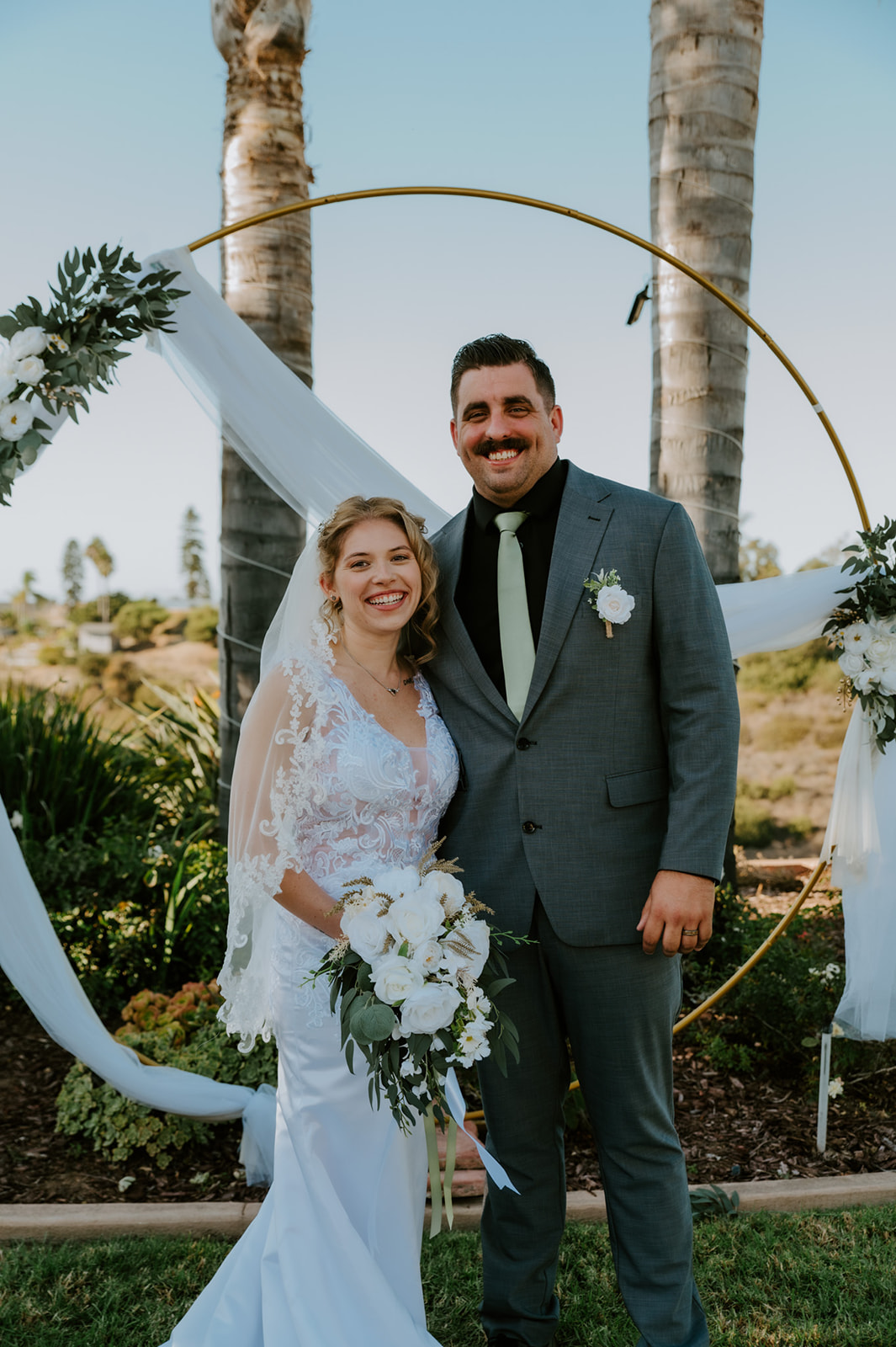 Bride and groom smiling together under a circular arch at their California Airbnb wedding ceremony before heading out for beach elopement photos.