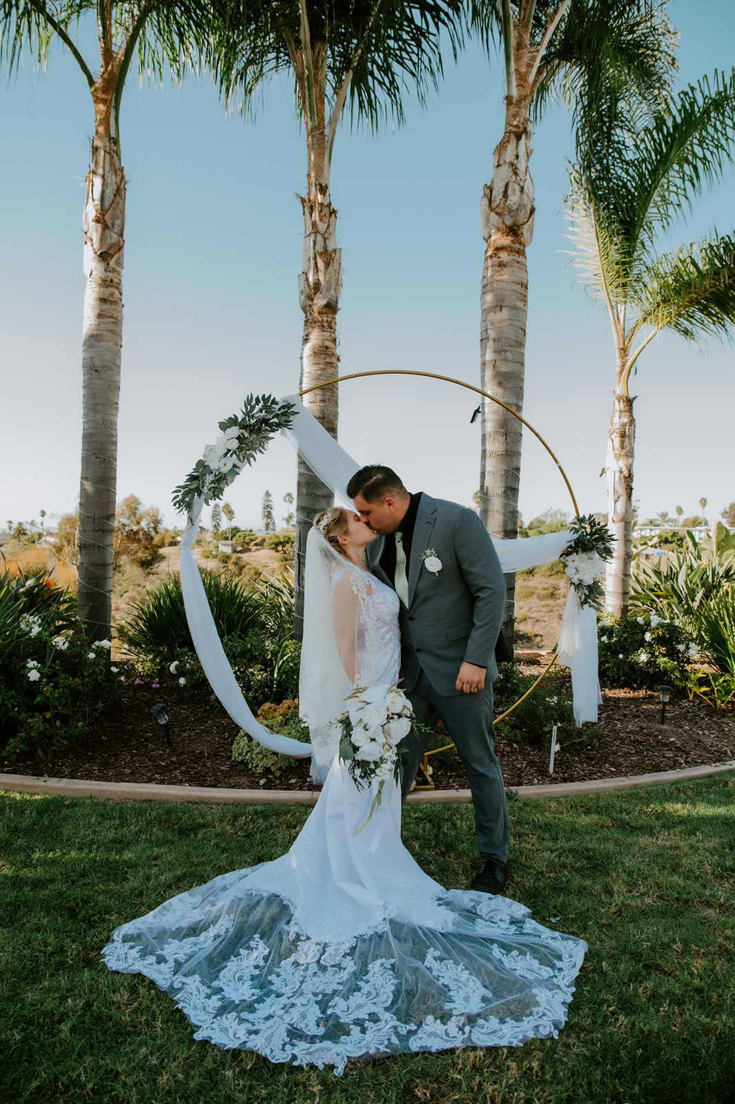 Bride and groom sharing a quiet kiss under palm trees after their family ceremony, part of a California elopement that blended an Airbnb wedding with beach portraits.