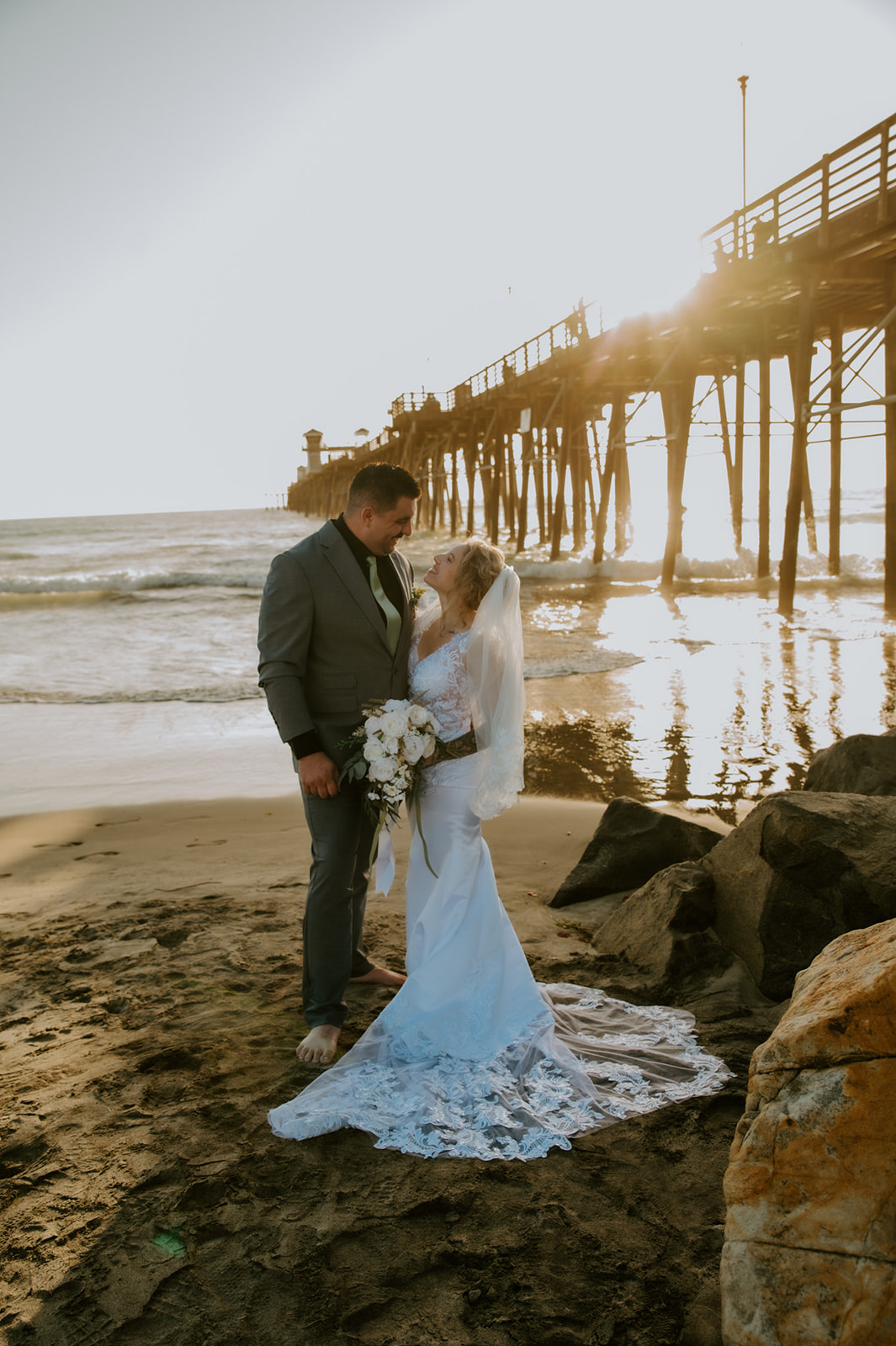 Bride and groom standing barefoot in the sand holding hands during golden hour beach elopement photos.