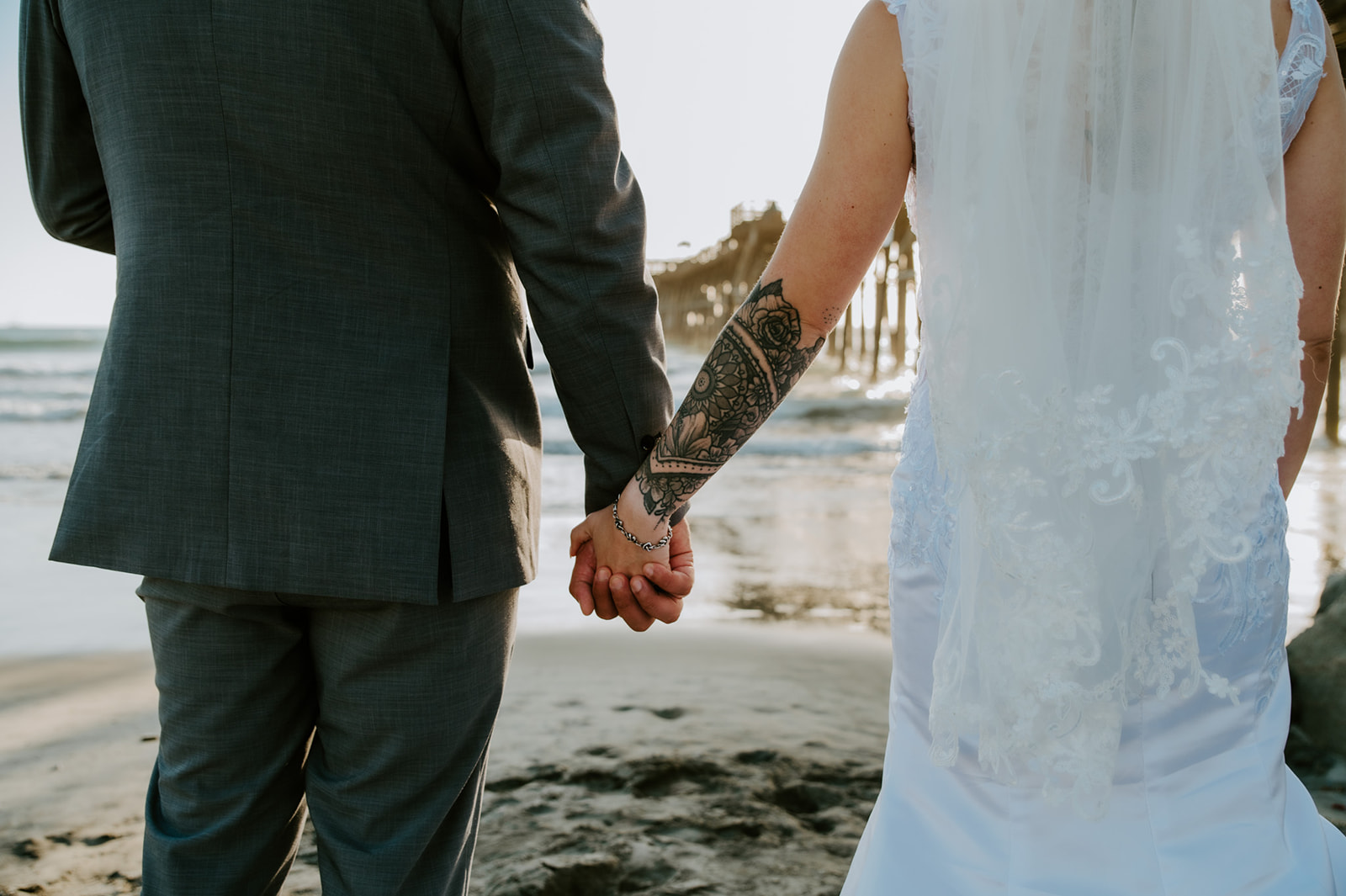 Bride and groom holding hands on the beach near the pier during golden hour, showing how to plan an elopement with family and still enjoy intimate beach elopement photos.