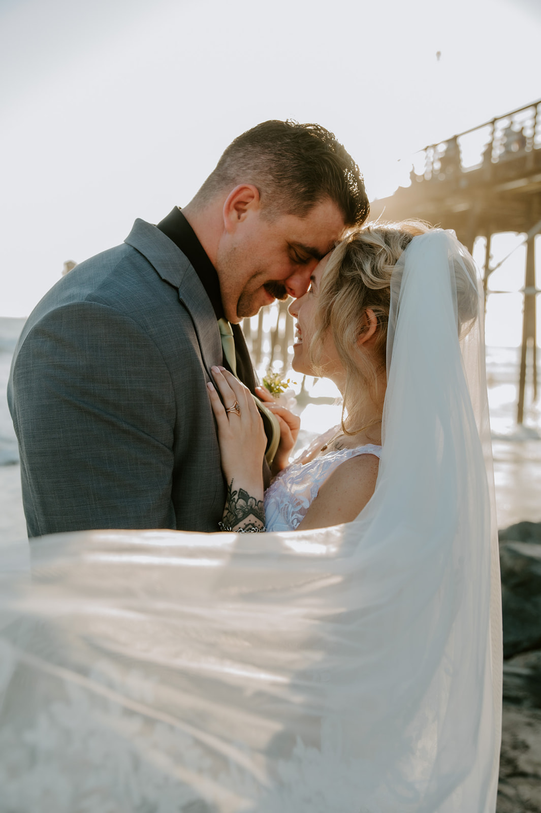 Couple embracing on the beach near the Oceanside pier during golden hour, a quiet moment from a California elopement planned with family present earlier in the day.