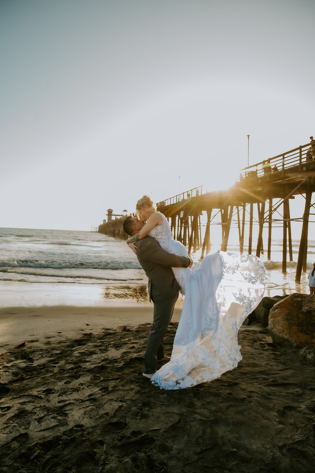 Groom lifting the bride on the beach at sunset after their family-focused elopement ceremony.