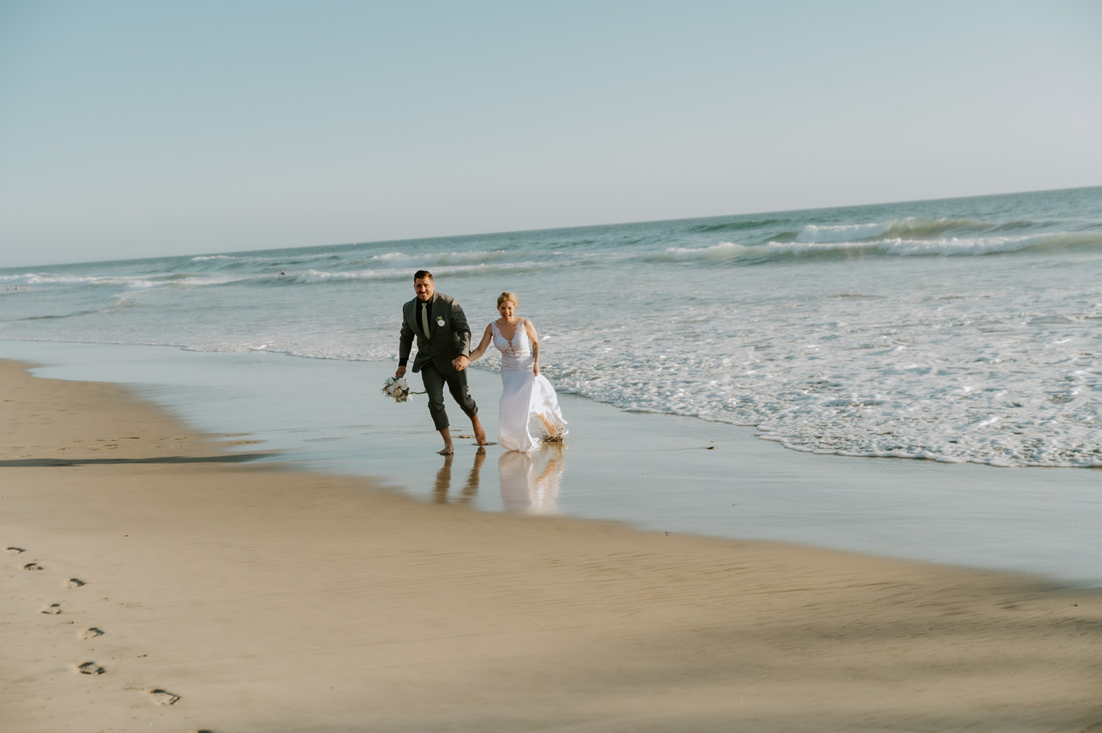Newlyweds running along the shoreline together after their ceremony, capturing the freedom of a relaxed California elopement.