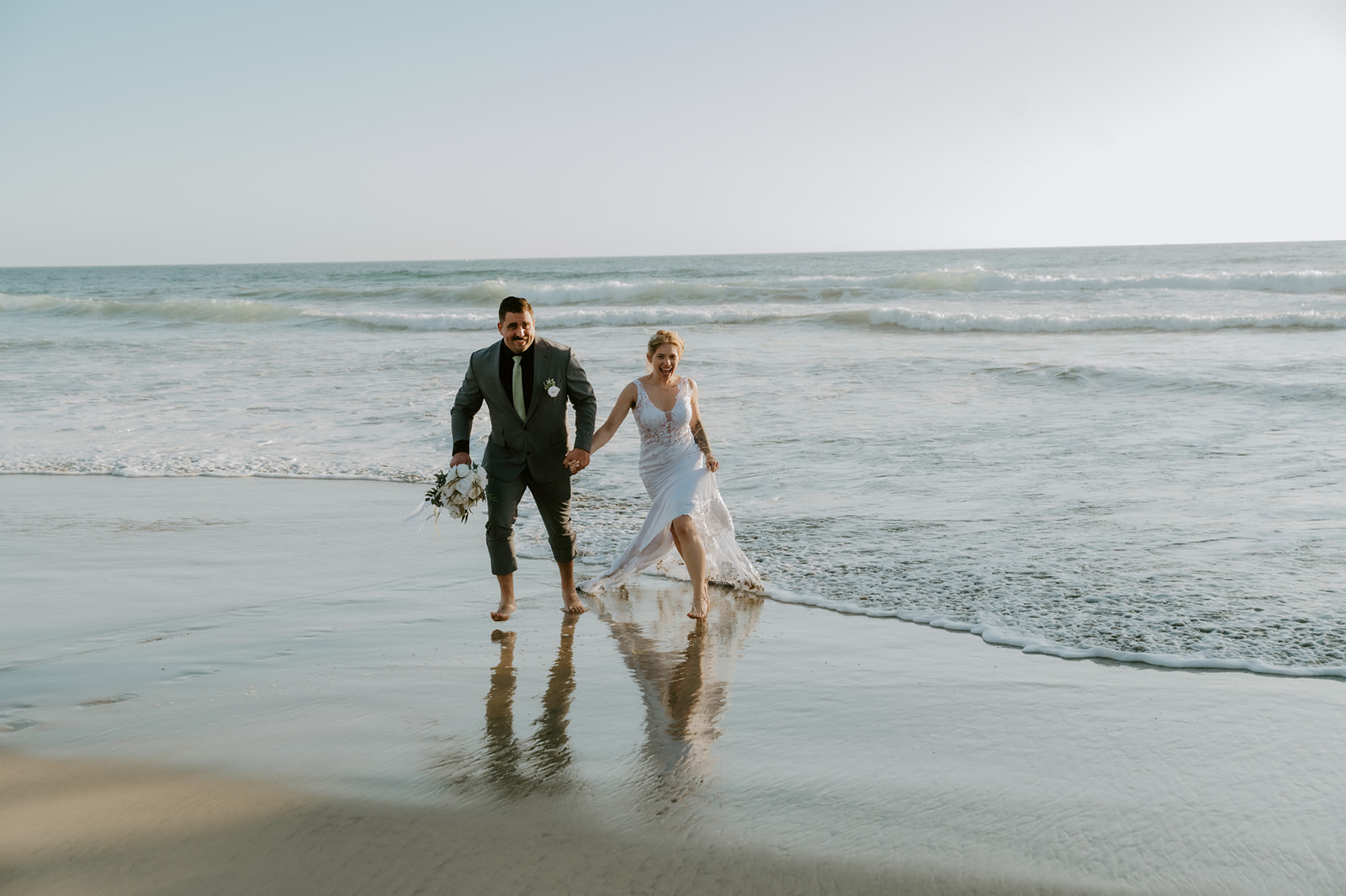 Bride and groom running hand in hand along the shoreline in Oceanside, capturing the freedom that comes from learning how to plan an elopement with family and space for adventure.