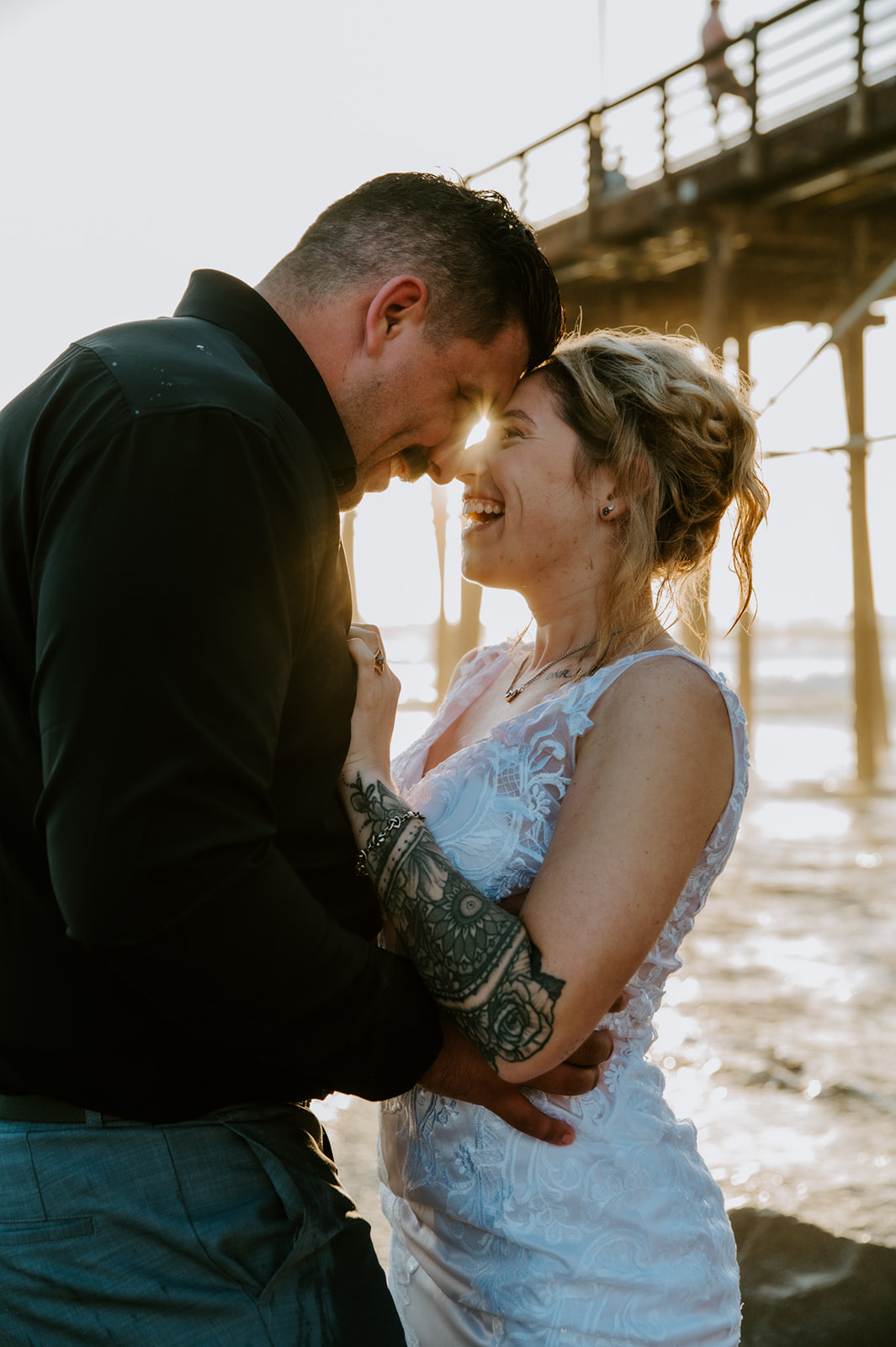 Close-up of the couple laughing forehead to forehead by the ocean, capturing the intimacy of eloping with family