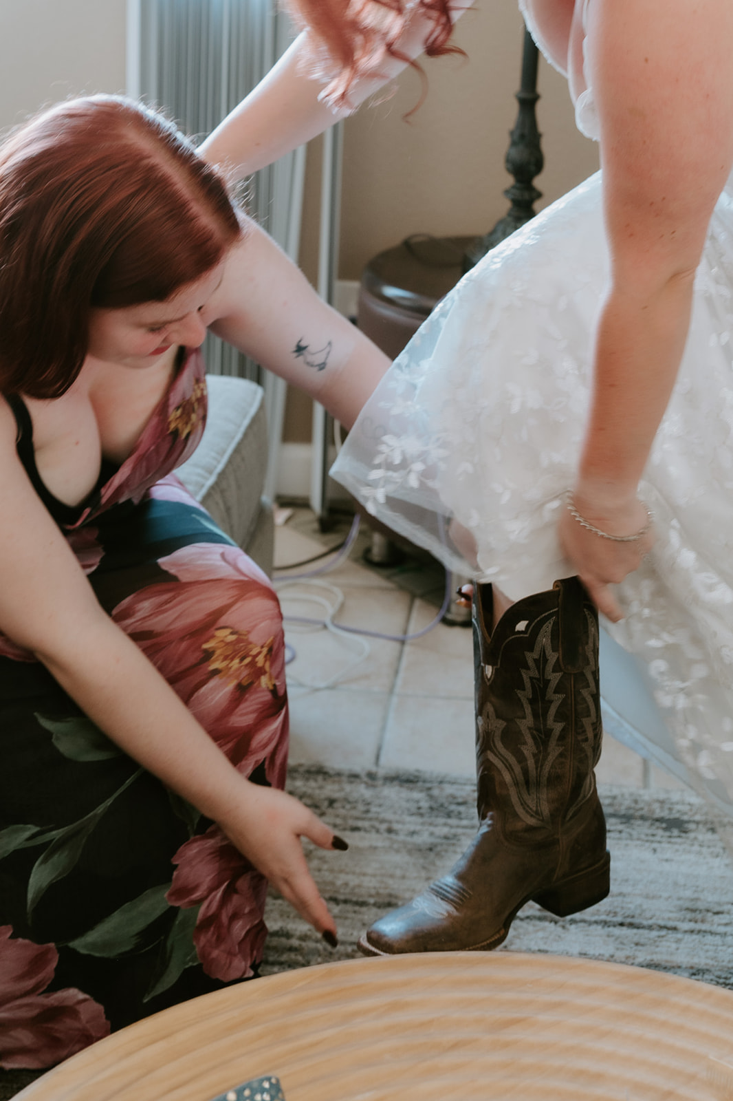 Family member helps bride into her cowboy boots before beach elopement, captured by California elopement photographer. 