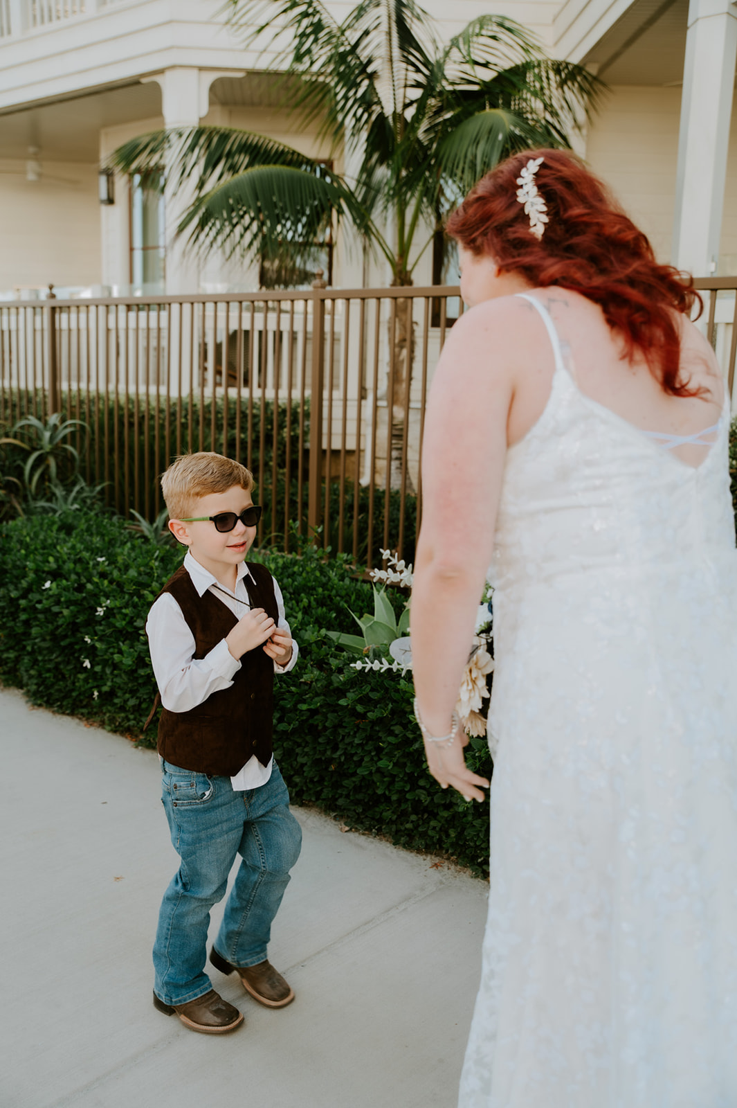 Young boy standing and smiling at his mom in her wedding dress while he sports sunglasses, captured by California elopement photographer. 
