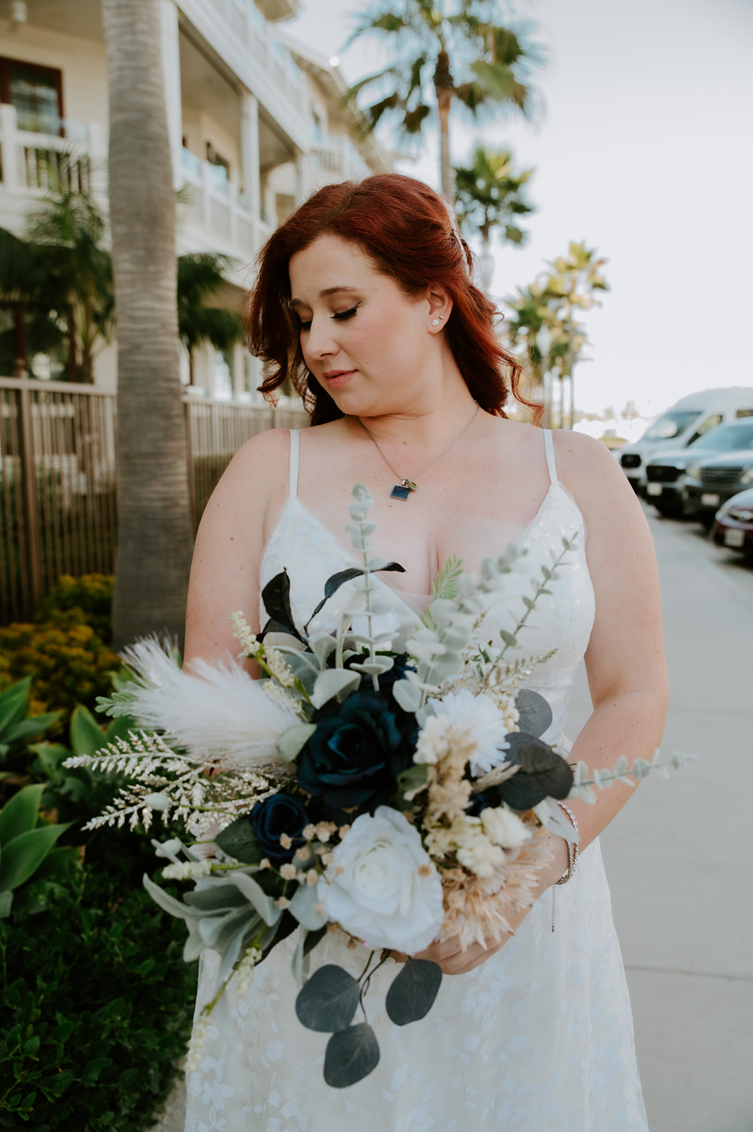 Bride holding her bouquet while walking along a palm-lined street after her beach elopement in California.