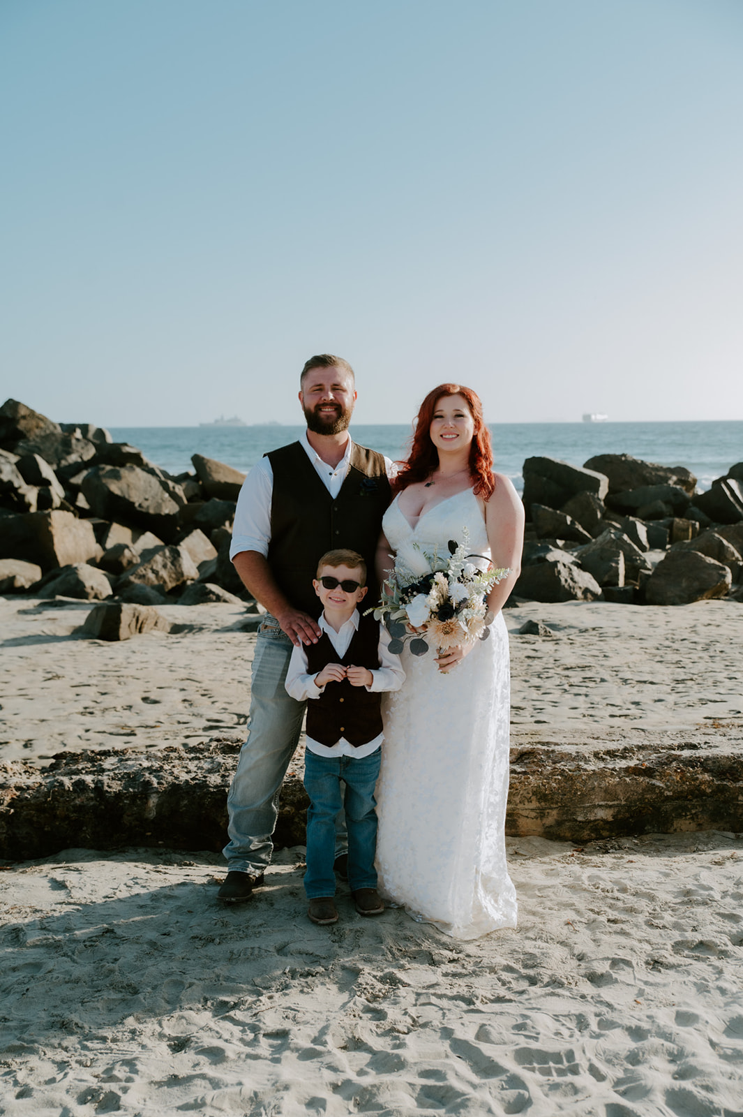 Young family standing together on beach smiling during family photos after bride and groom eloped on the beach.