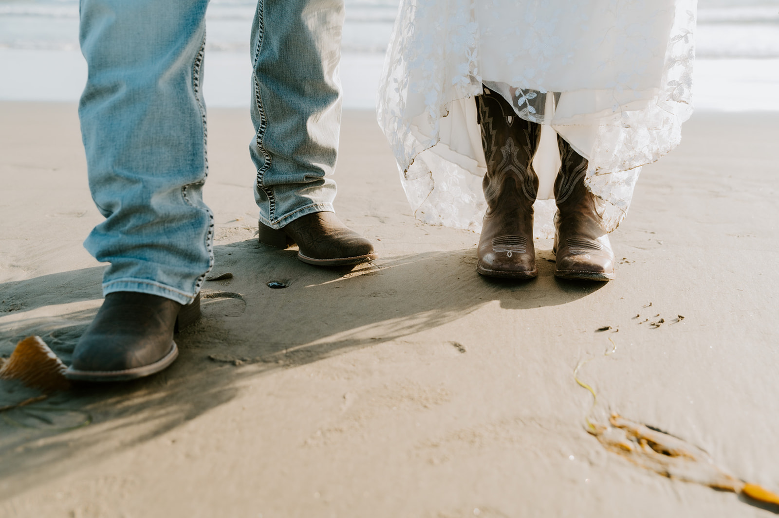 Close-up of the couple’s boots and wedding attire standing on the sand after their coastal elopement.