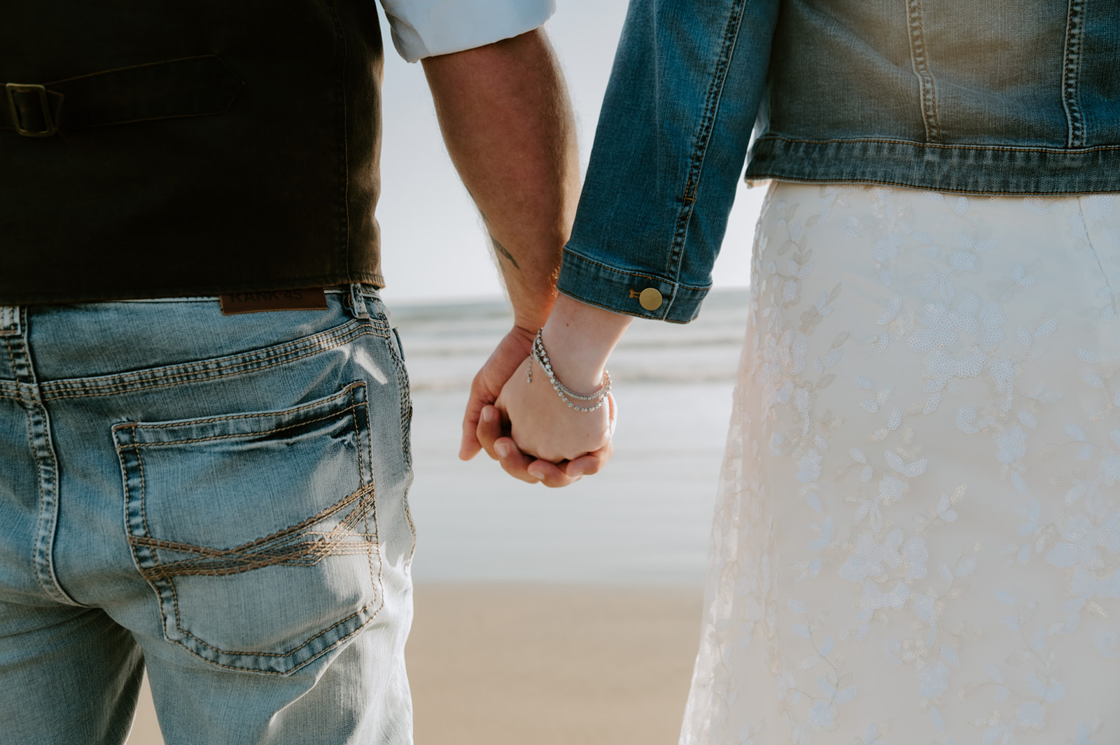 Close-up of the couple holding hands on the beach, showing wedding attire details during their elopement.