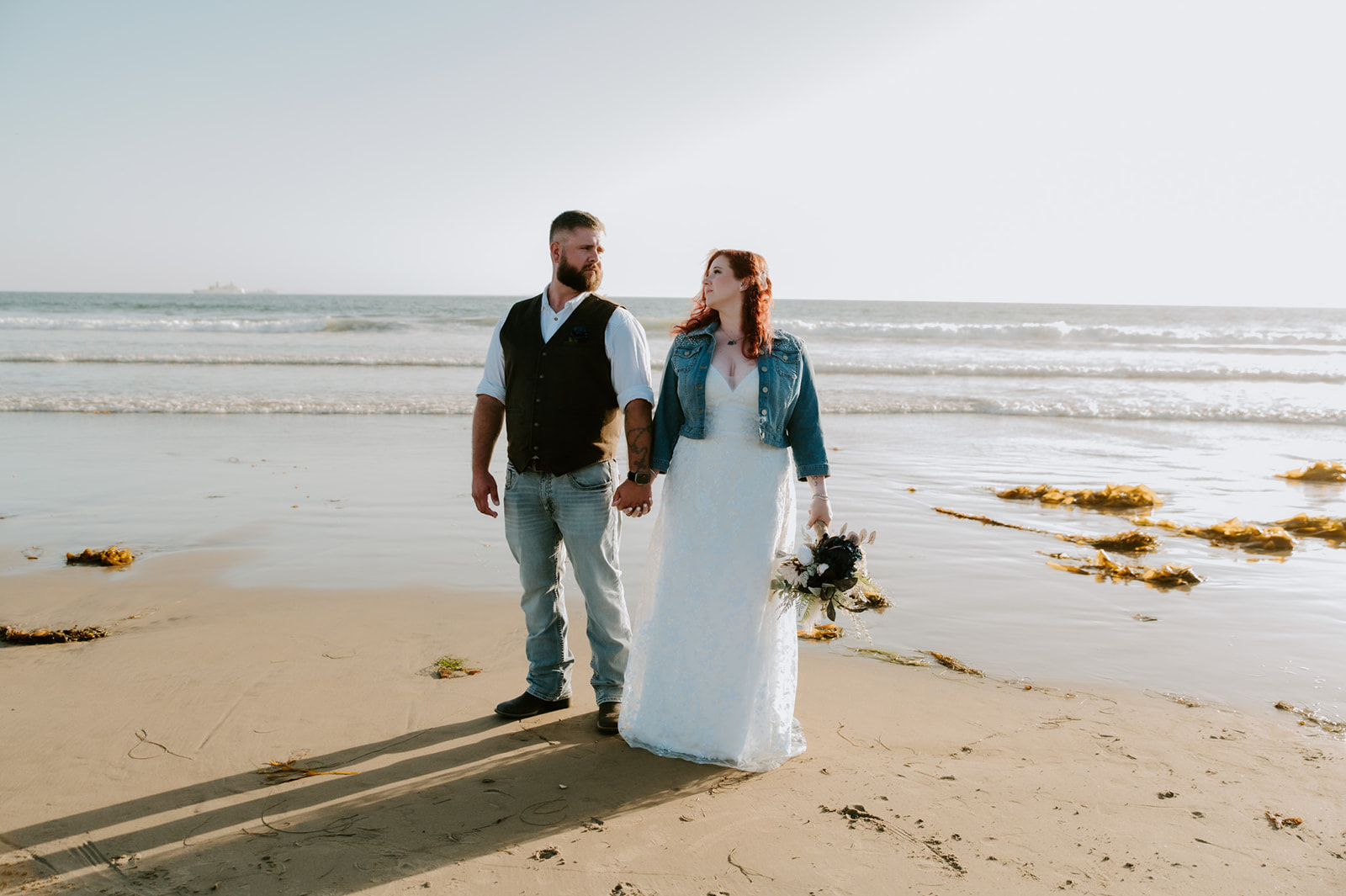 Newly married couple lookikng at one another holding hands with the ocean behind them captured by California elopement photographer. 