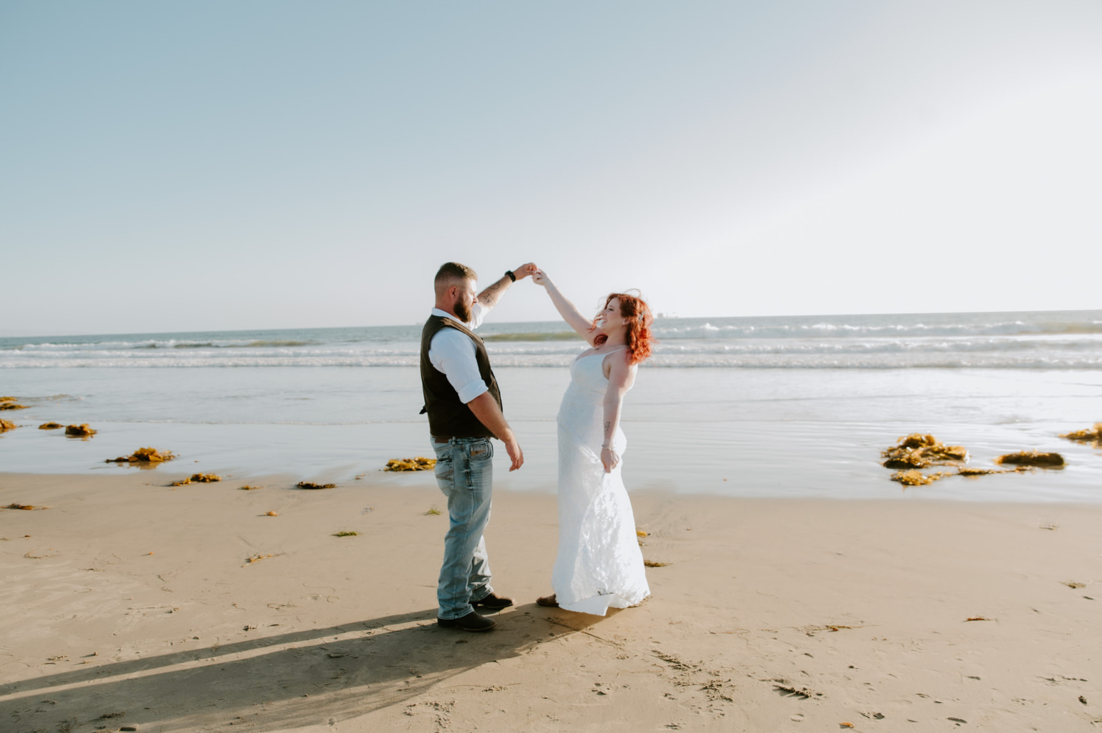 Bride and groom dancing together on the beach after their elopement, ocean waves in the background.