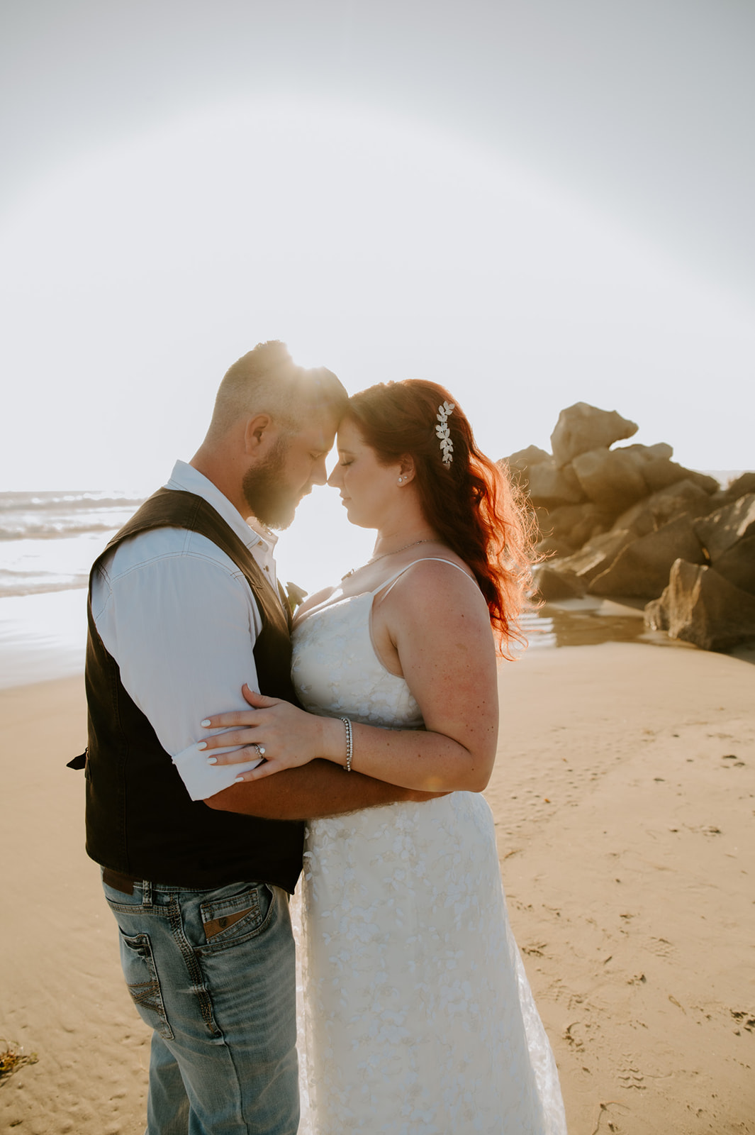 Bride and groom embracing on a sandy California beach with ocean waves behind them, photographed by a California elopement photographer