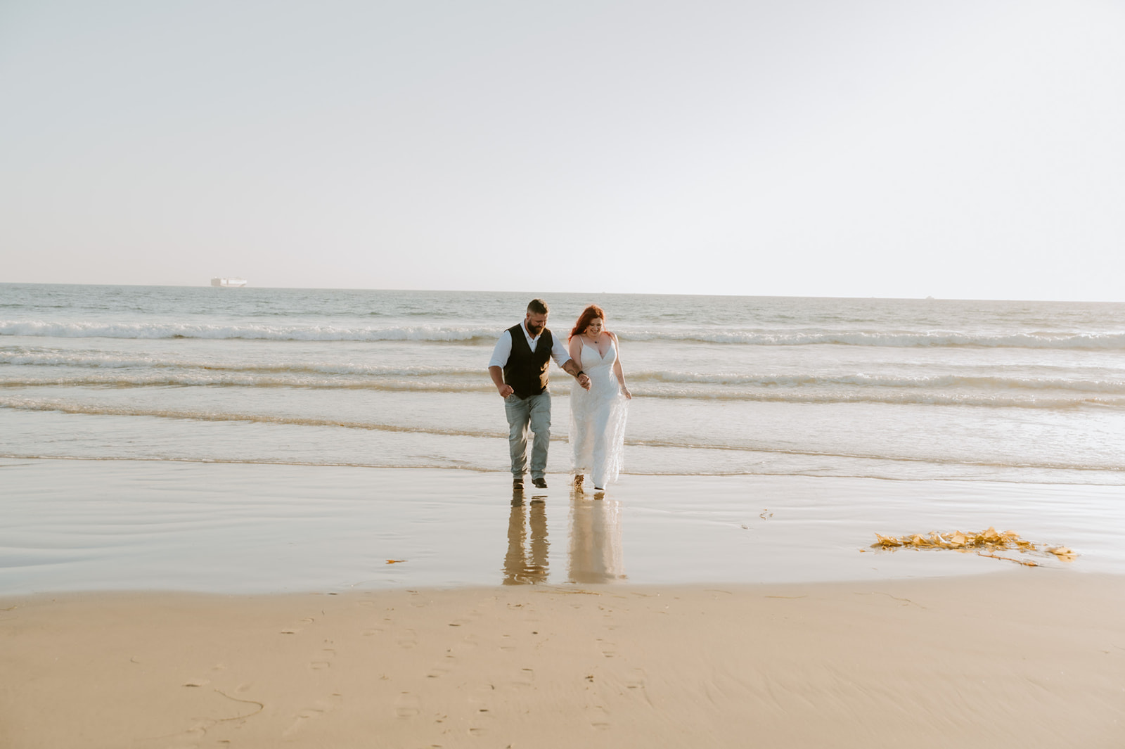 Elopement couple walking hand in hand along the shoreline with reflections in wet sand, photographed by a California elopement photographer