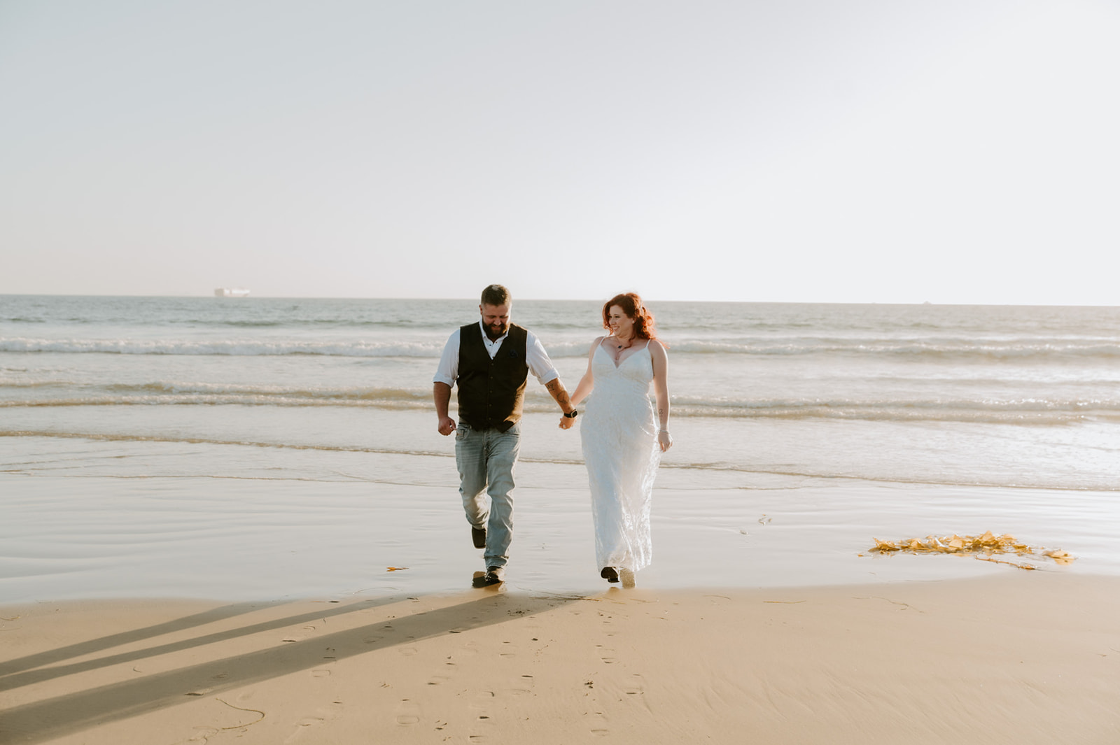 Elopement couple walking toward the camera along the beach as waves roll in behind them
