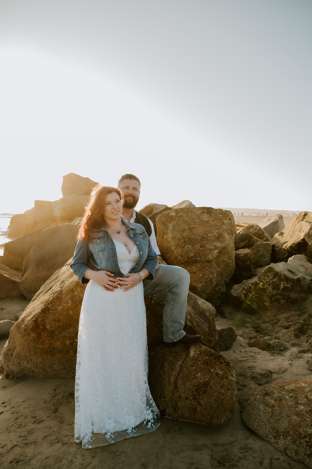 Bride leaning into groom while seated on beach rocks during a laid-back California elopement at golden hour