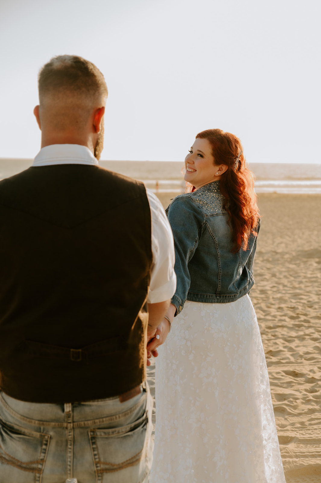 Bride holding groom's hand and leading him to the beach. 
