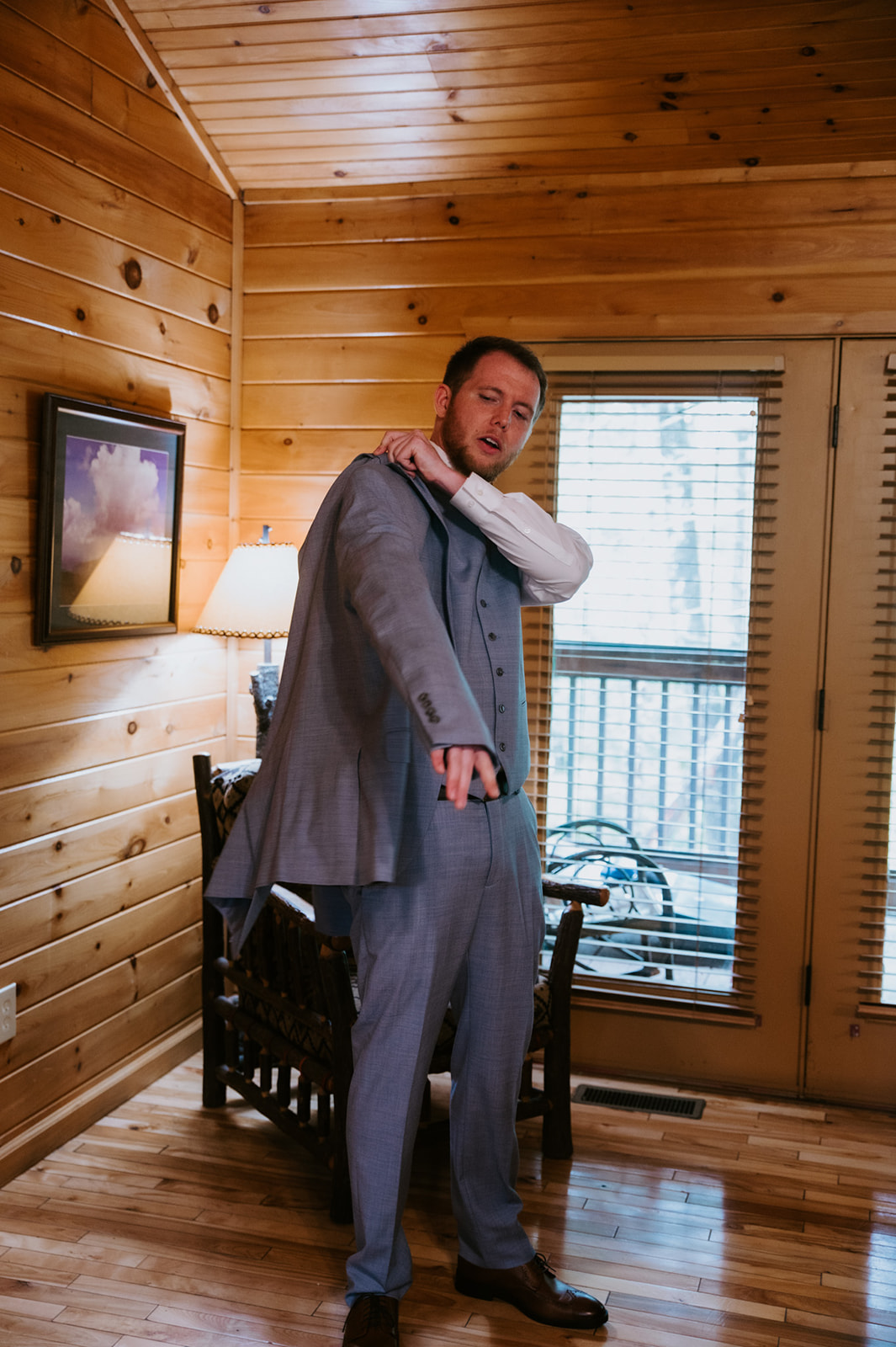 Groom getting ready in a wood cabin during a Smoky Mountain Elopement, adjusting his suit jacket in warm window light before the ceremony.