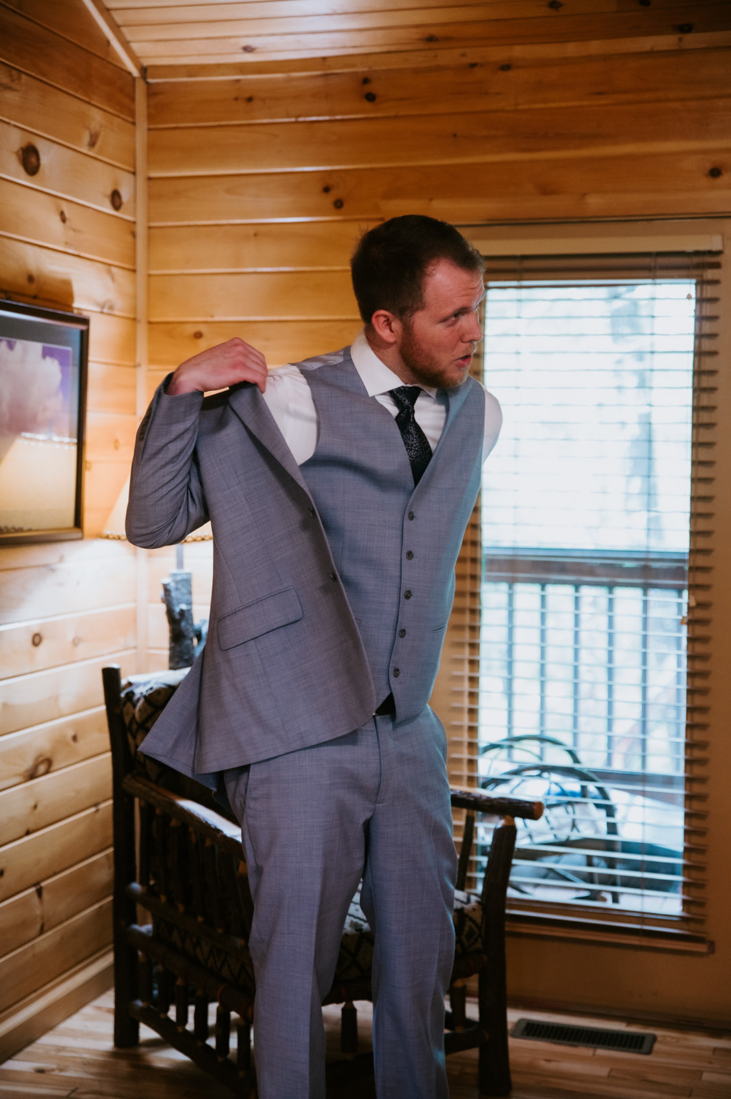Groom putting on his suit jacket inside a wooden cabin during Smoky Mountain elopement preparations.