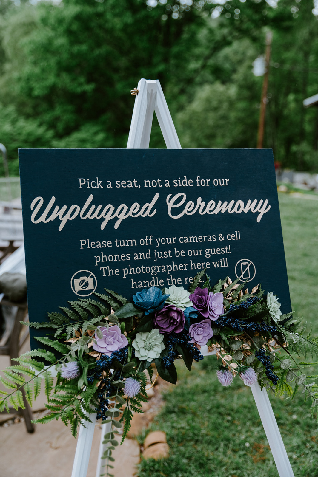 Unplugged ceremony sign decorated with florals at an outdoor Smoky Mountain wedding ceremony.