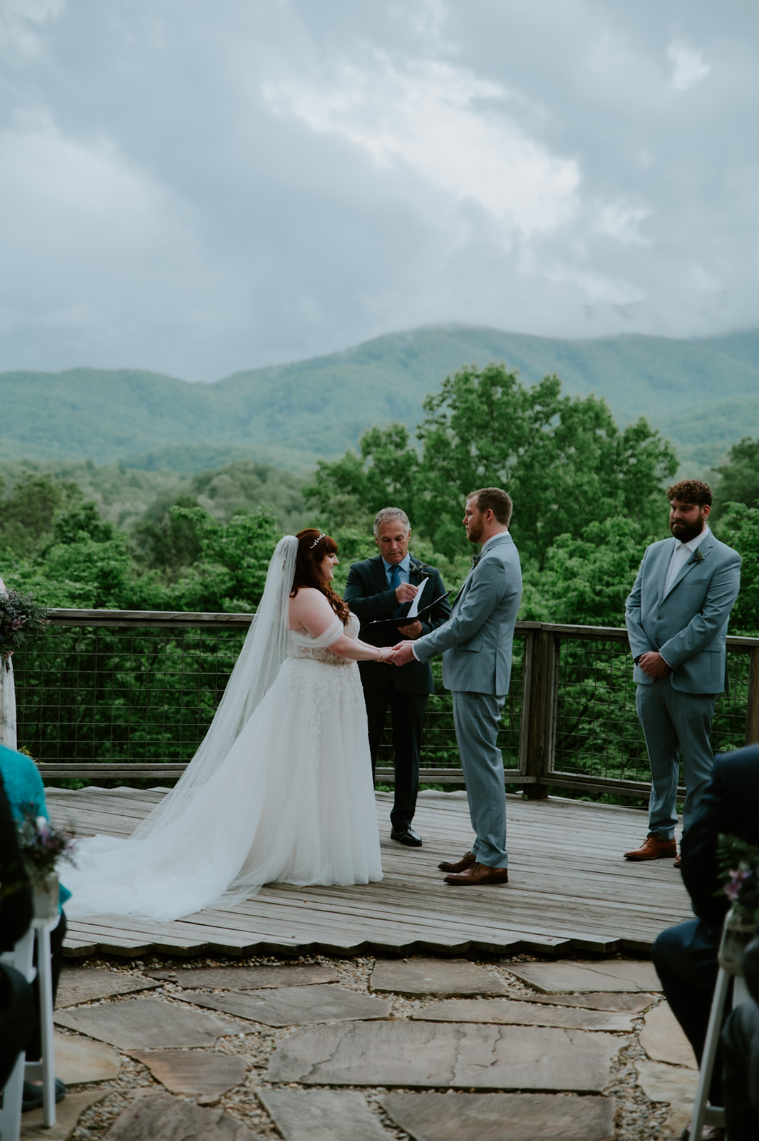 Outdoor Smoky Mountain Elopement ceremony on a wooden deck overlooking the mountains, with the couple holding hands as they exchange vows.