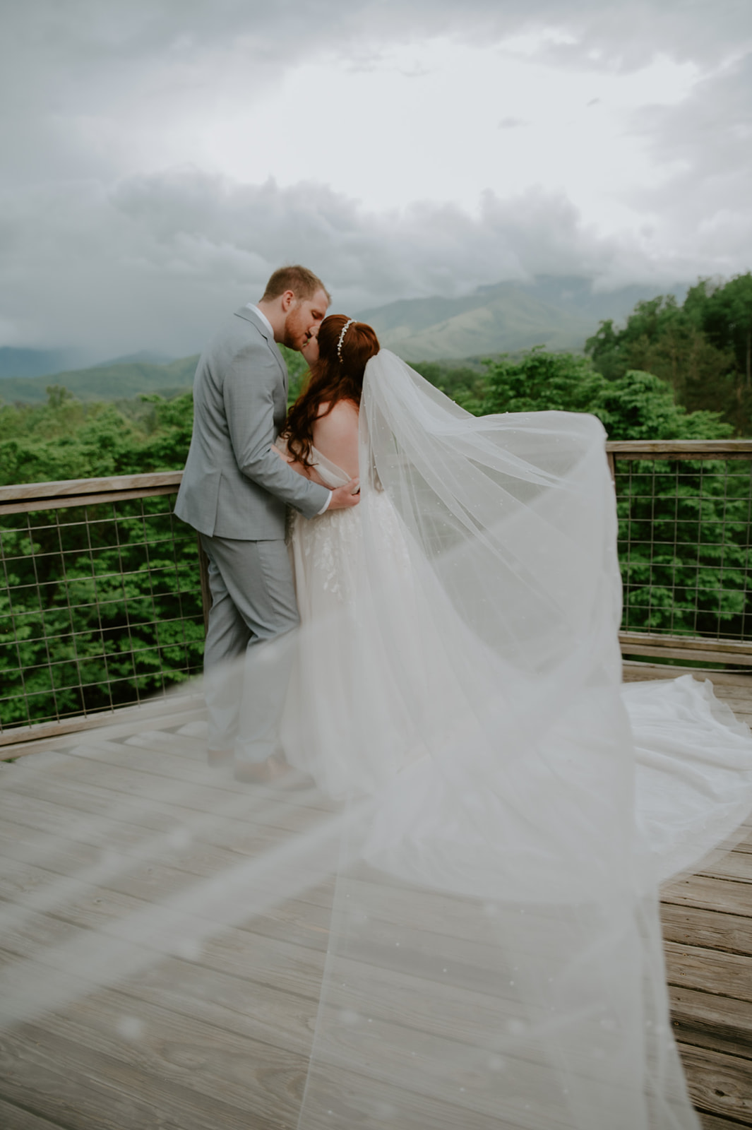 Couple kissing softly on a mountain overlook with fog and layered hills in the background