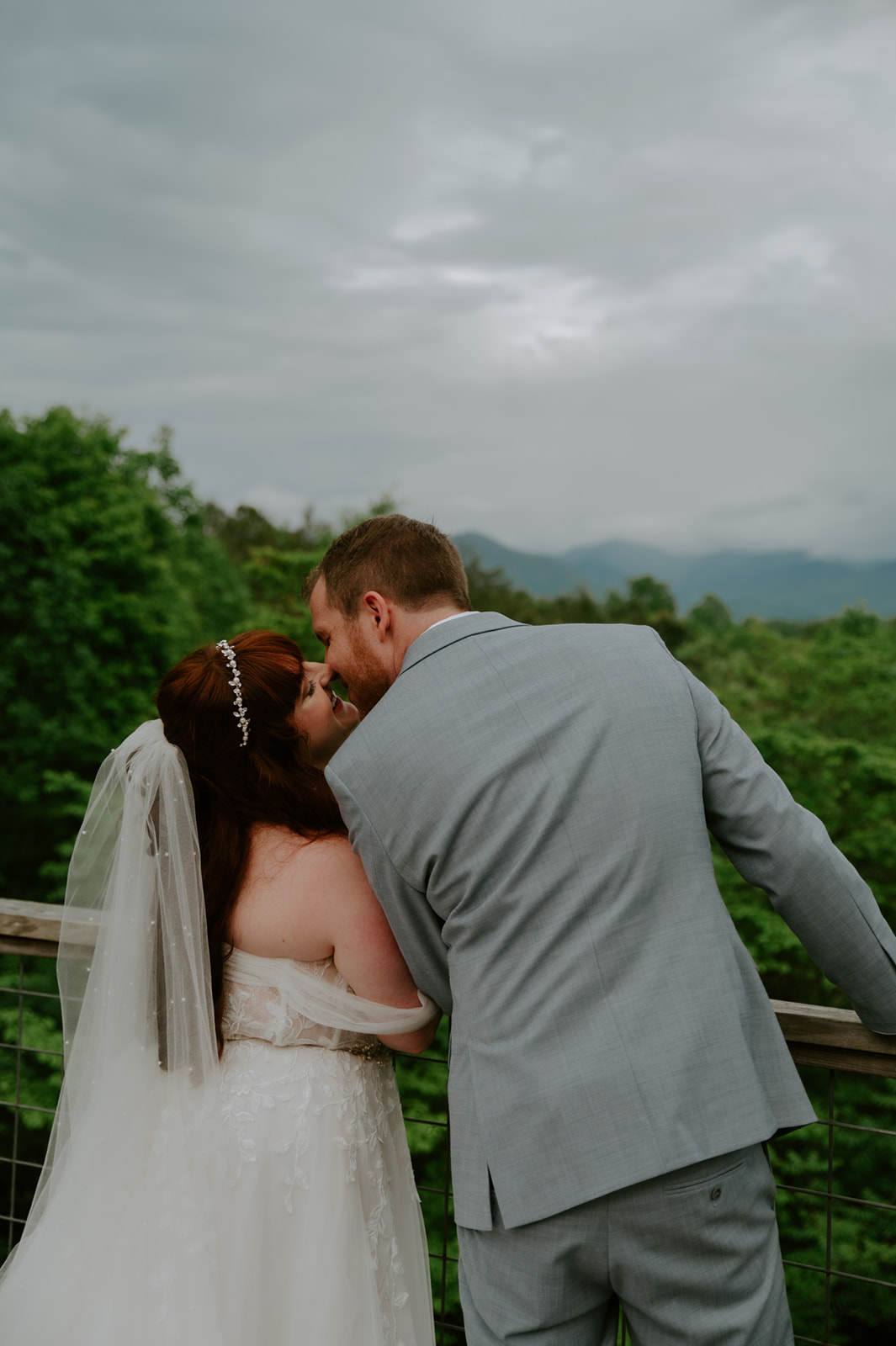Bride and groom kissing at a mountain overlook with dramatic clouds rolling in behind them.