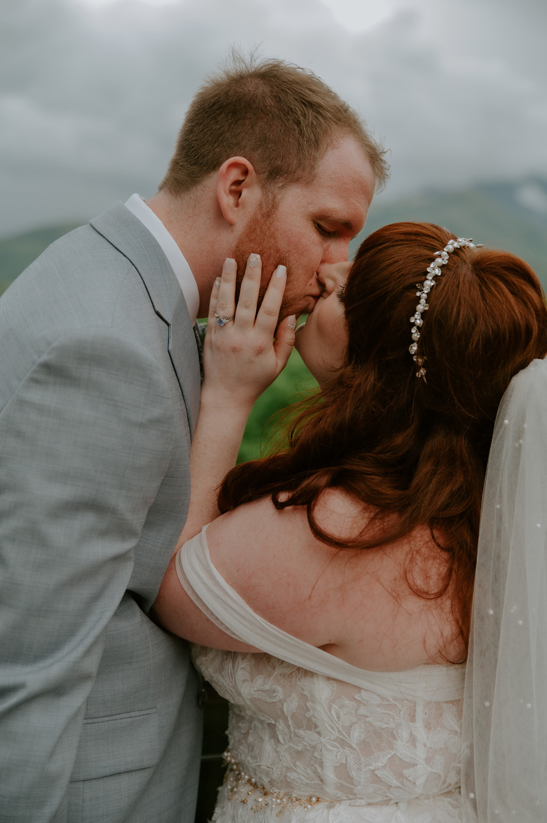 Close-up of the bride and groom sharing their first kiss during the ceremony, surrounded by soft mountain light and greenery.